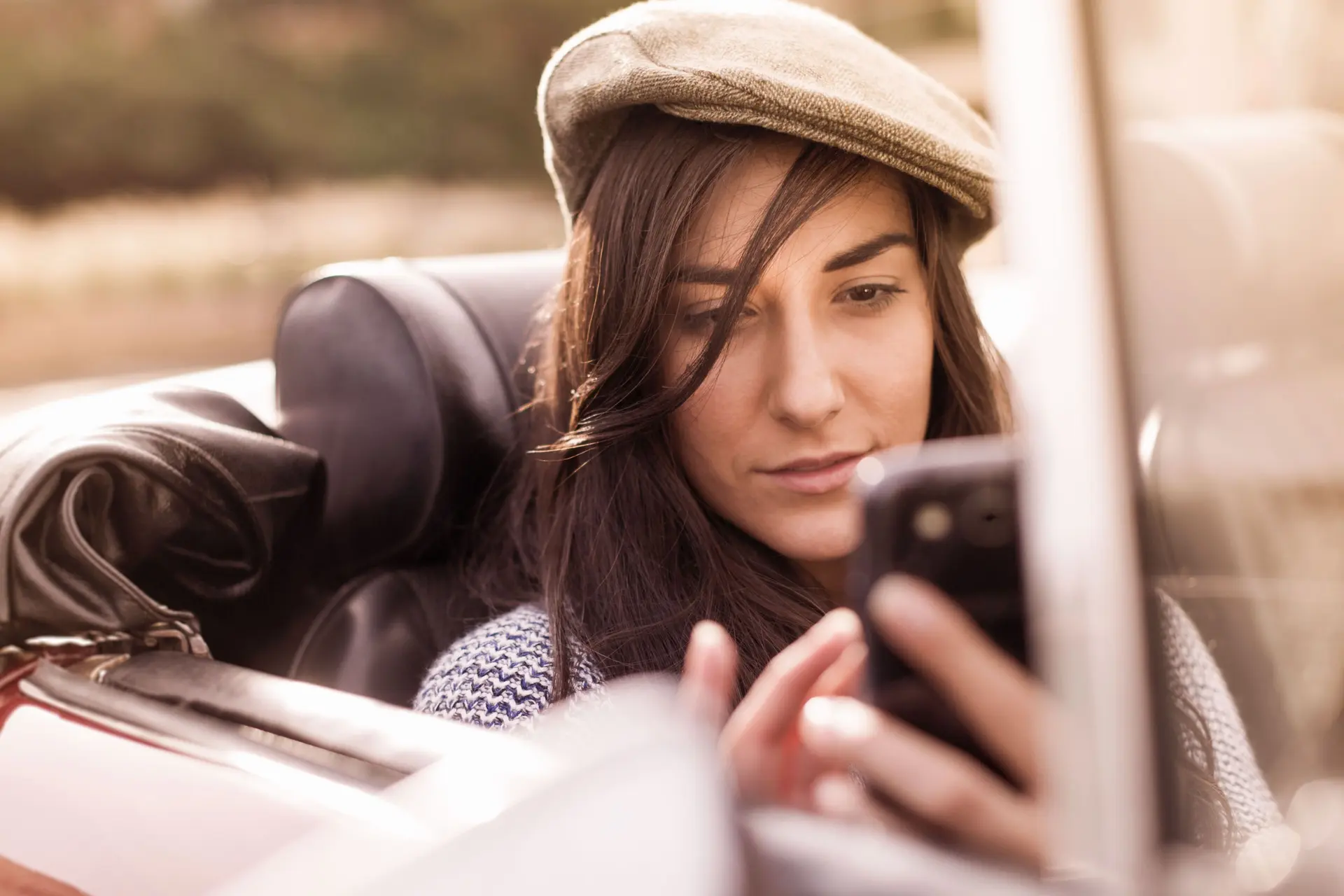 Junge Frau mit einer Schirmmütze sitzt in einem Cabriolet und verwendet ihr Smartphone