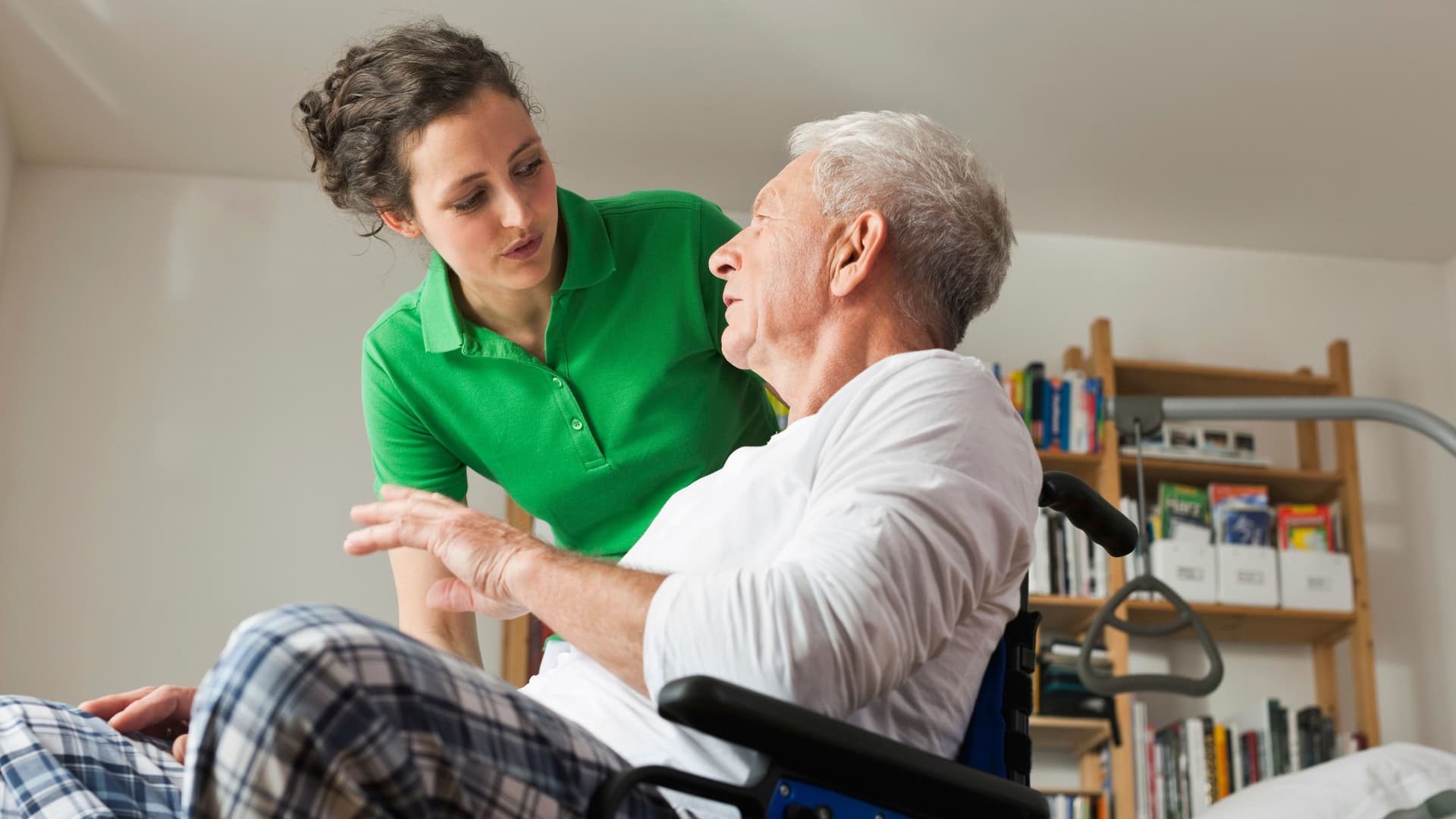 Junge Frau spricht mit älteren Mann imRollstuhl