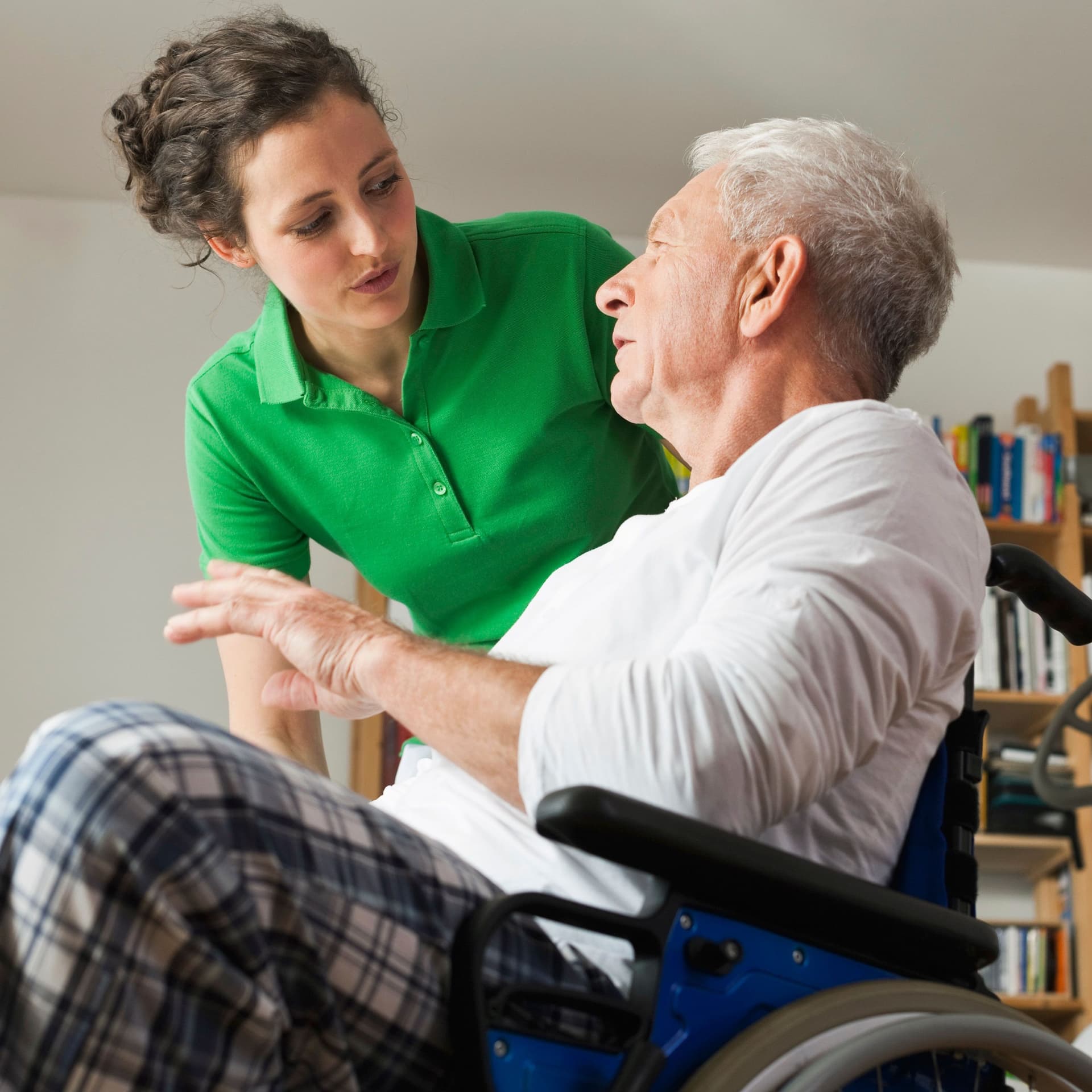 Junge Frau spricht mit älteren Mann imRollstuhl