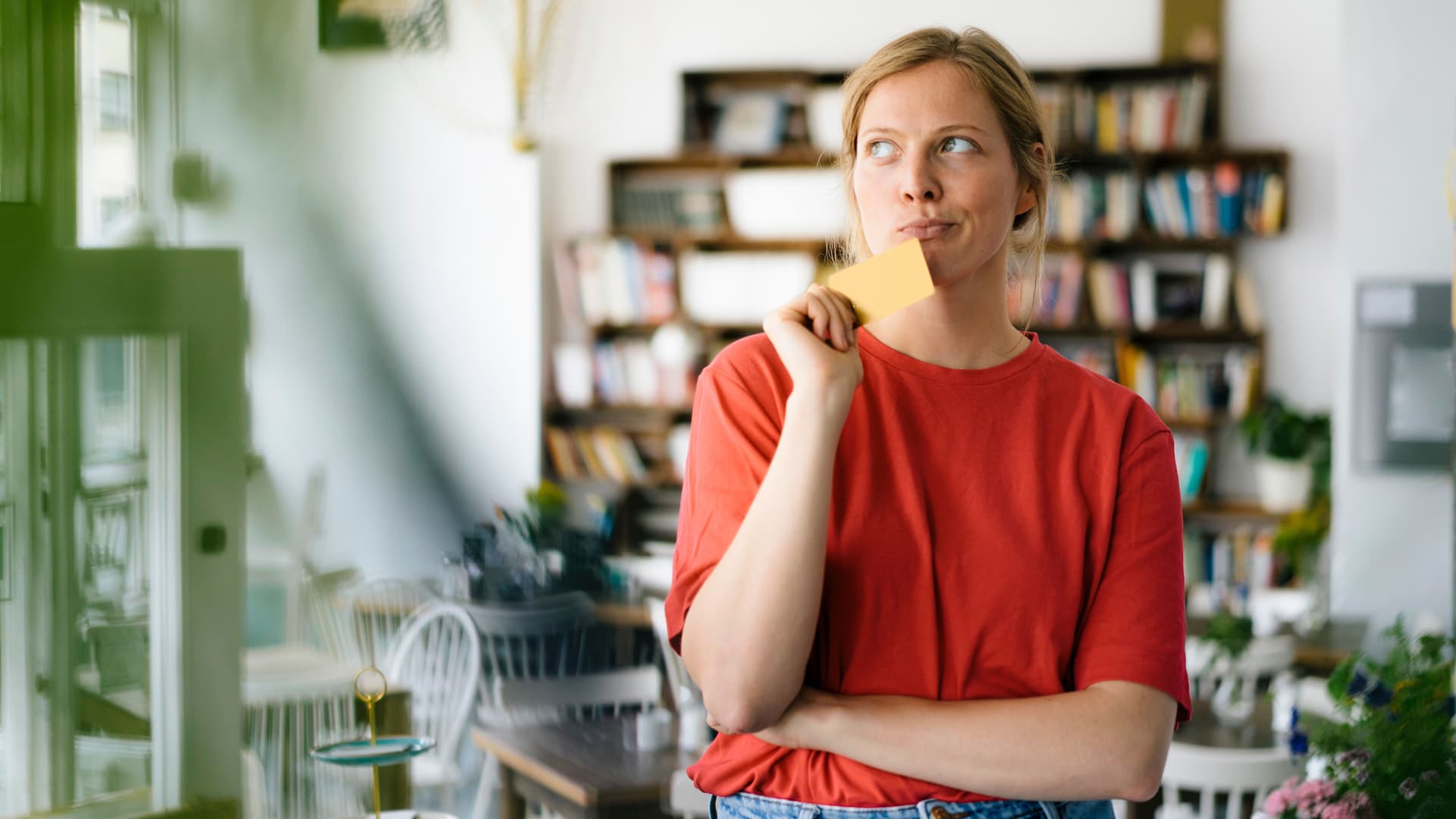 Junge Frau steht in ein cafe, und überlegt während sie ihre Kreditkarte in der Hand hält.