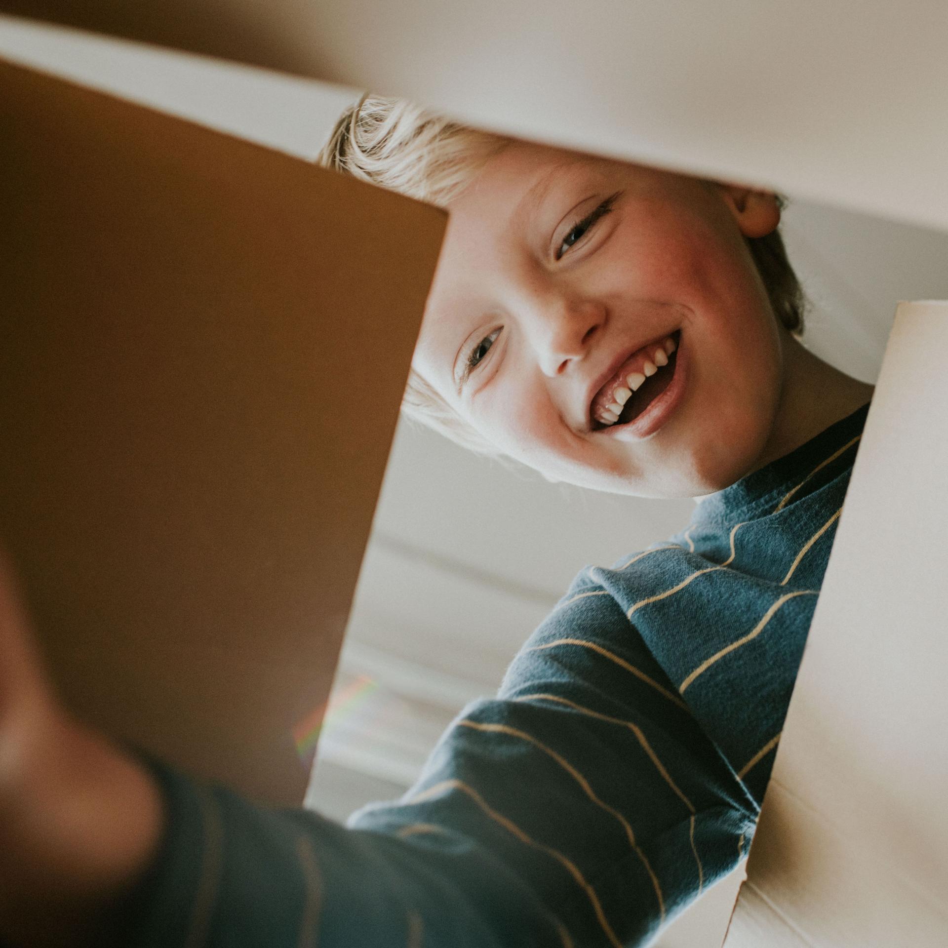 Aus der Froschperspektive aufgenommenes Bild von einem lachenden Jungen, der einen Karton öffnet. 