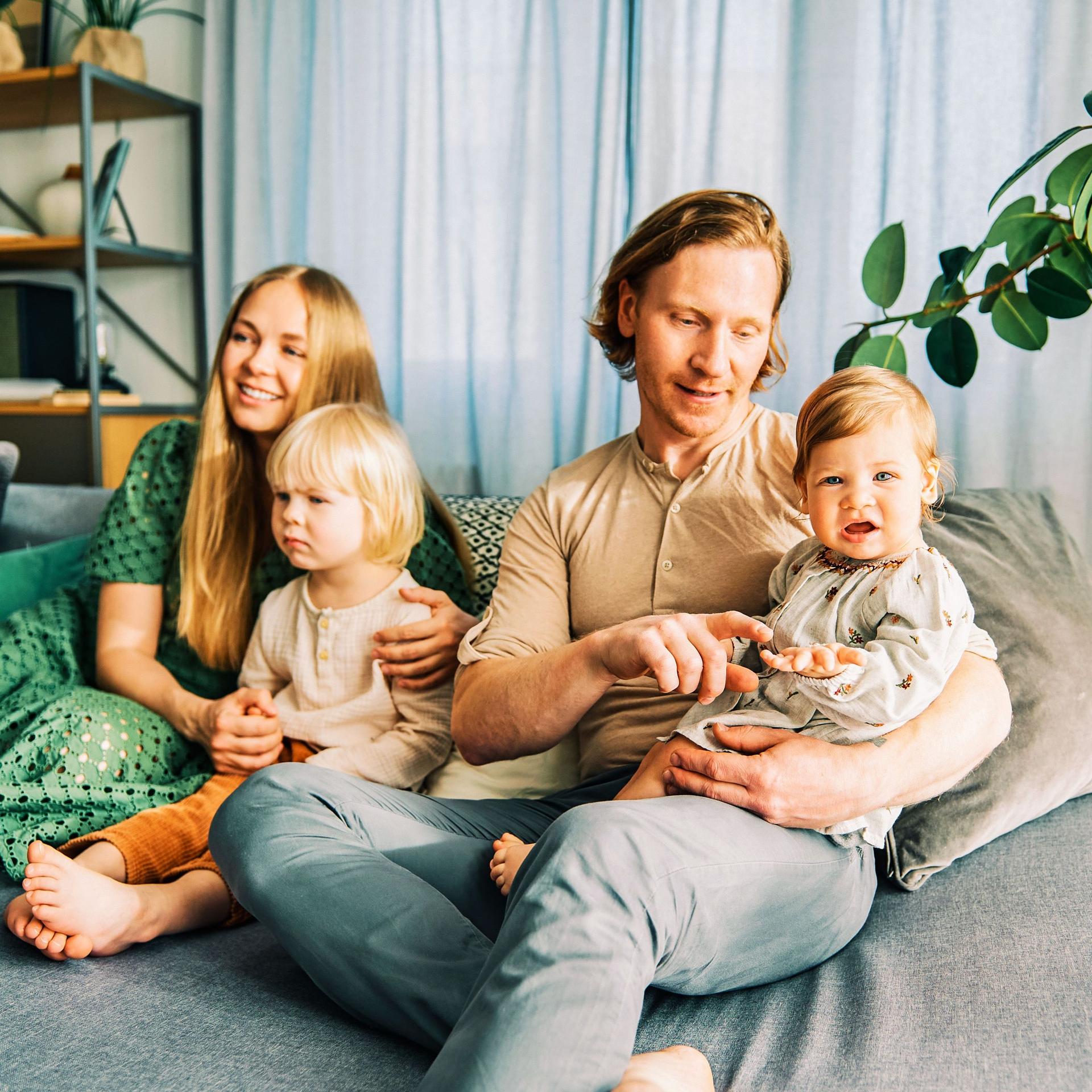 Mann und Frau mit zwei Kindern sitzen auf einem Sofa. 