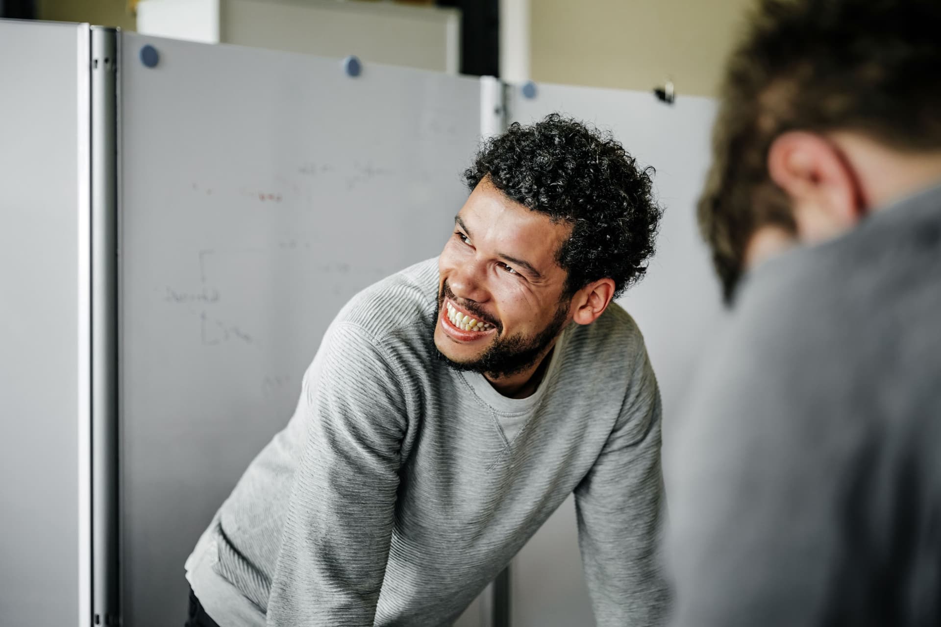Mann steht vor einer Magnetwand in einem Meeetingraum und blickt lachend zur Seite.
