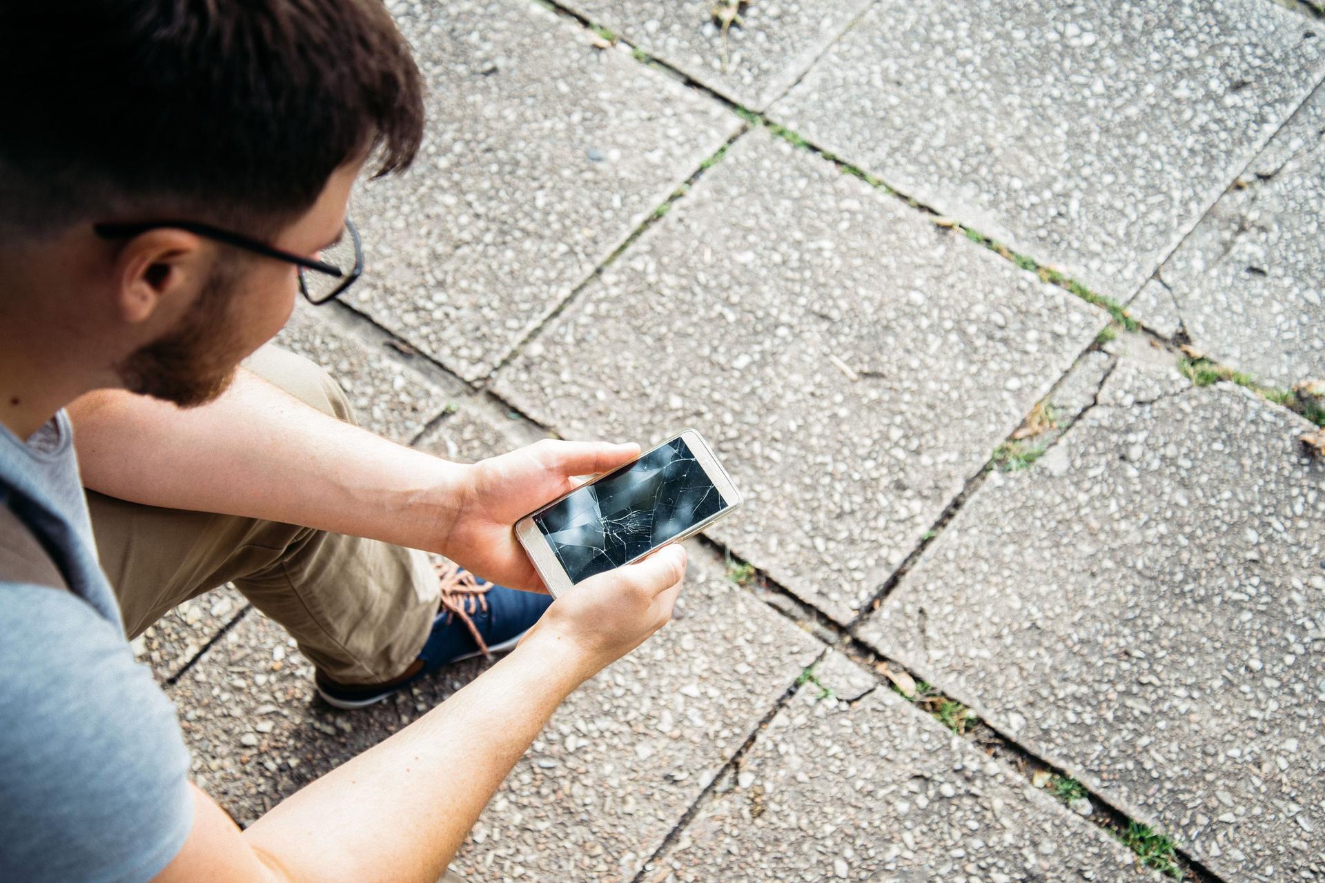 Ein junger Mann hält ein Smartphone mit einem zerbrochenen Bildschirm.