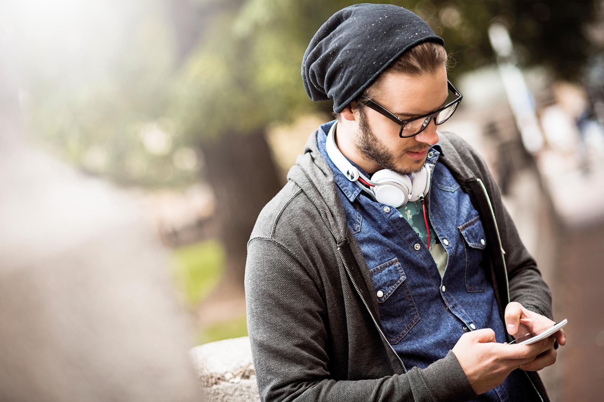 Junger Mann mit Mütze und Kopfhörern tippt auf einem Smartphone.