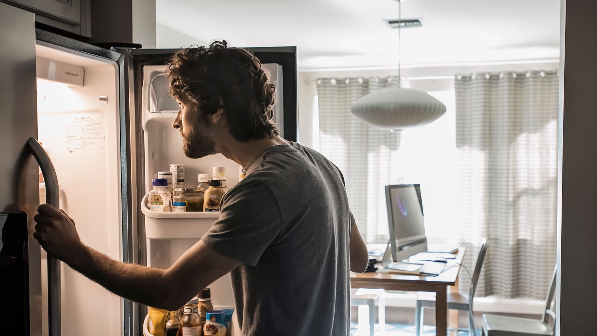 Ein Mann steht vor einem geöffneten Kühlschrank und schaut hinein.