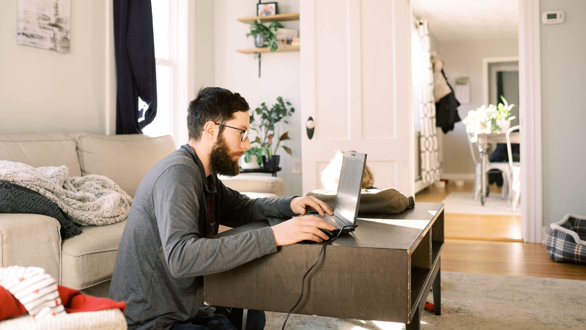 Ein junger Mann sitzt auf dem Wohnzimmerboden und arbeitet an einem Laptop