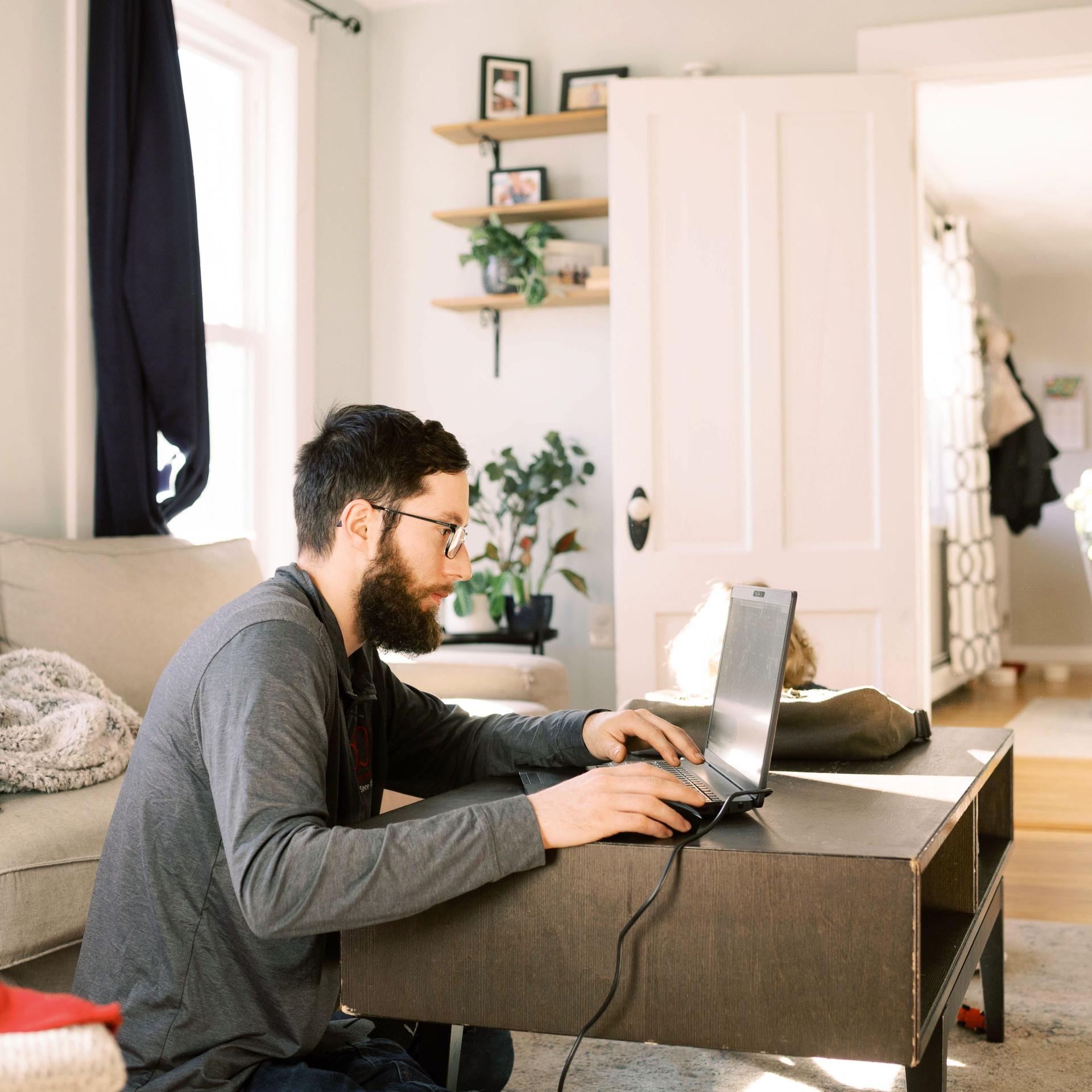 Ein junger Mann sitzt auf dem Wohnzimmerboden und arbeitet an einem Laptop