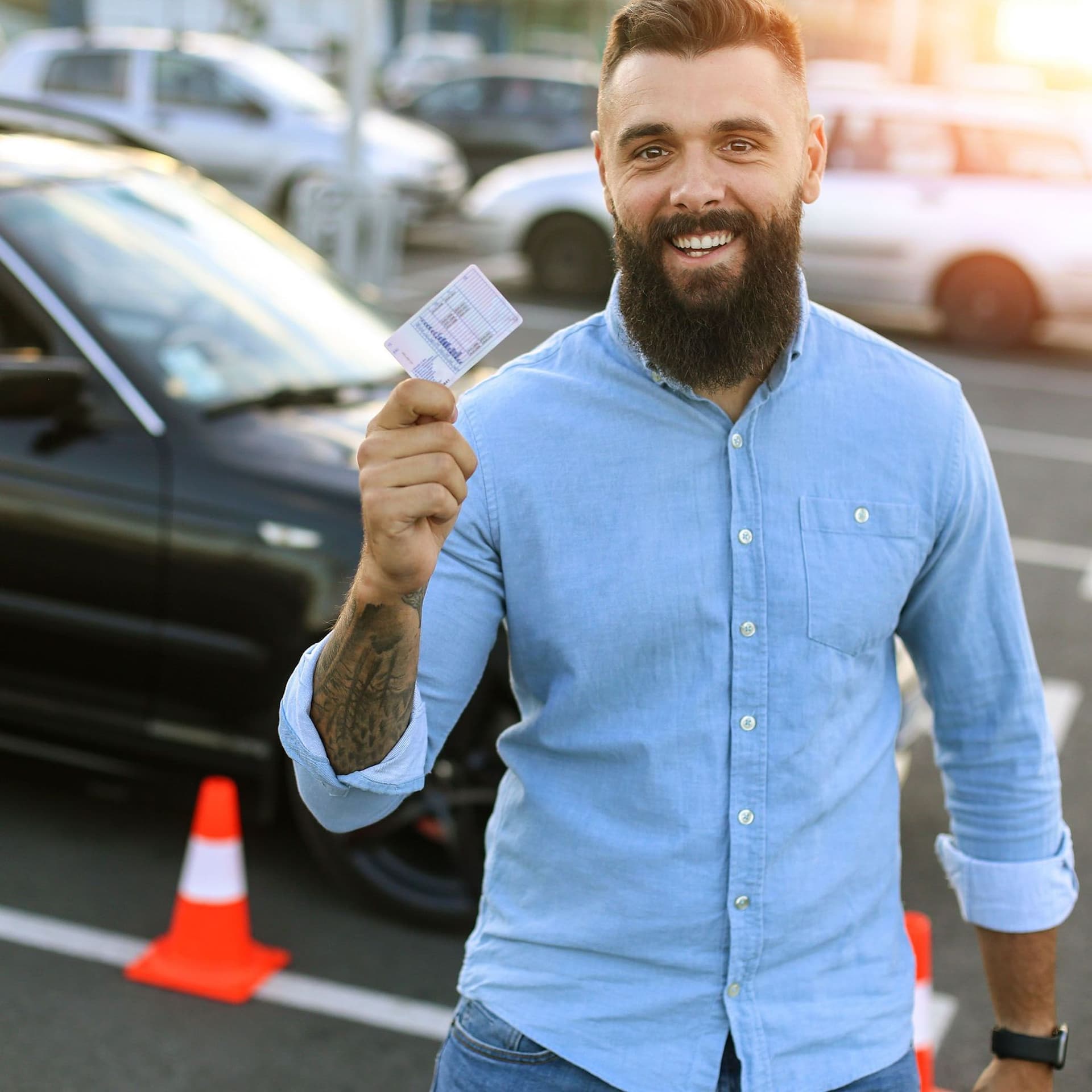 Junger Mann steht auf einem Parkplatz und hält lachend seinen Führerschein in die Kamera