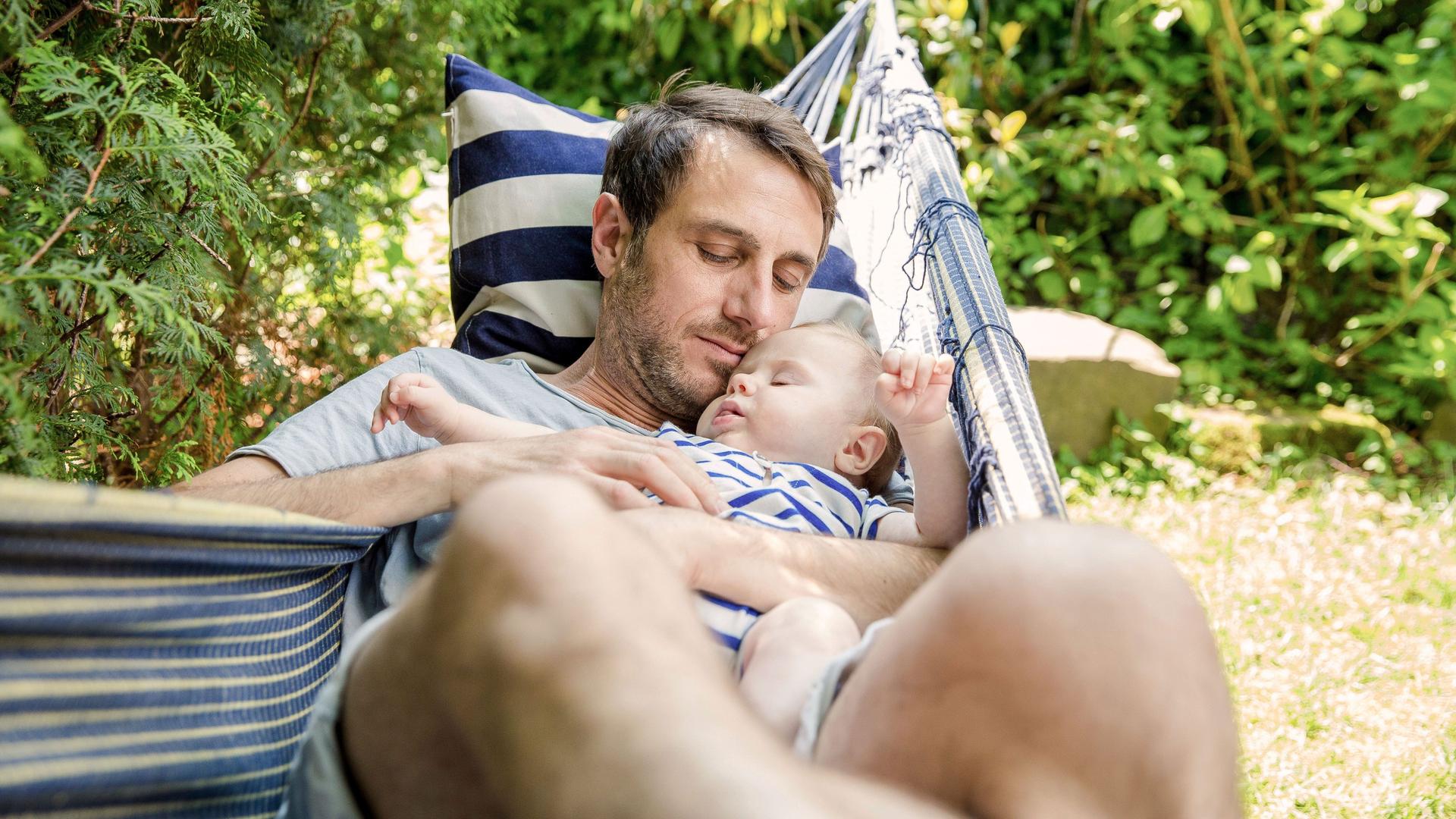 Porträt eines Vaters mit Baby, das in der Hängematte schläft, bei sommerlichen Temperaturen.