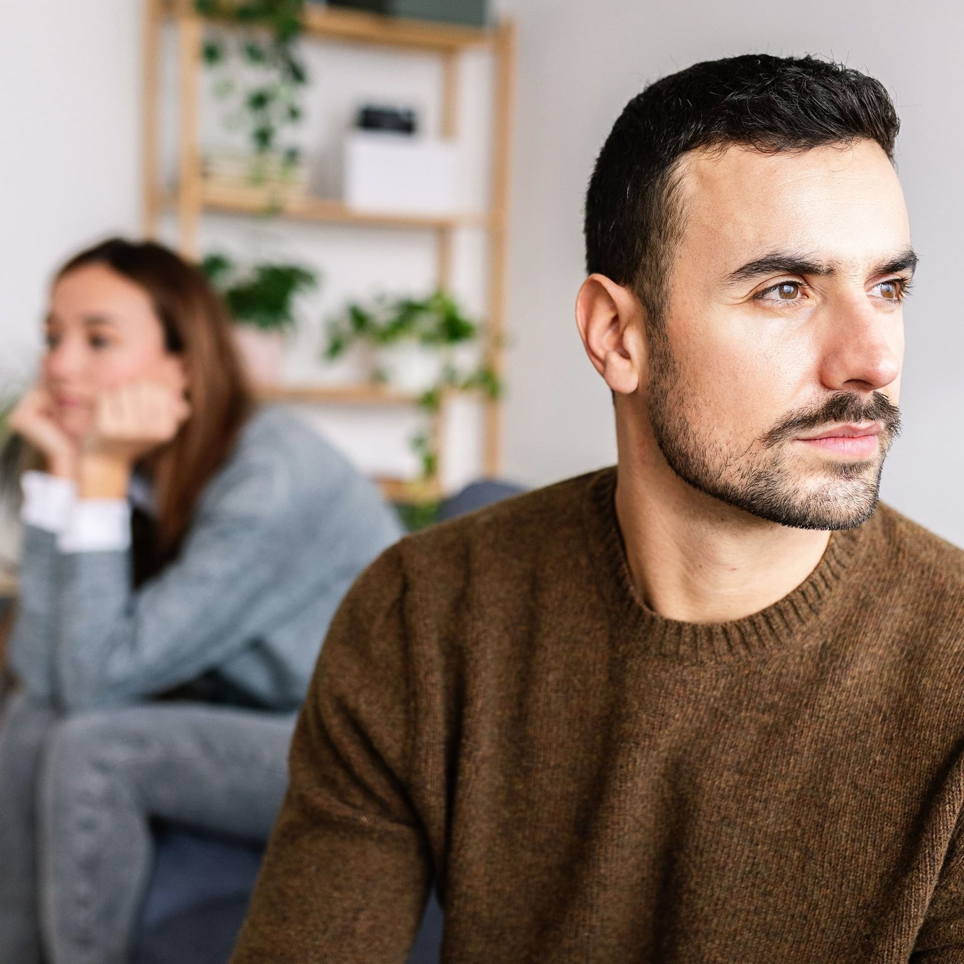 Junges Paar sitzt distanziert auf einem Sofa. Einer junger Mann sitzt vorne und blickt zur Seite, während die Frau im Hintergrund in die andere Richtung blickt.