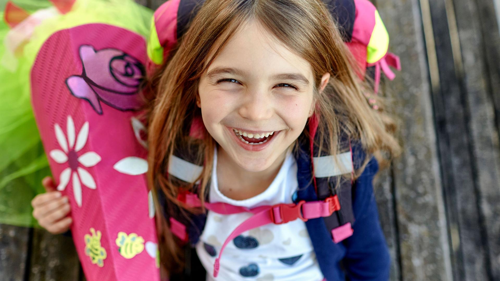 Porträt eines glücklichen Mädchens mit Schultüte und Schulranzen auf Holzplanken