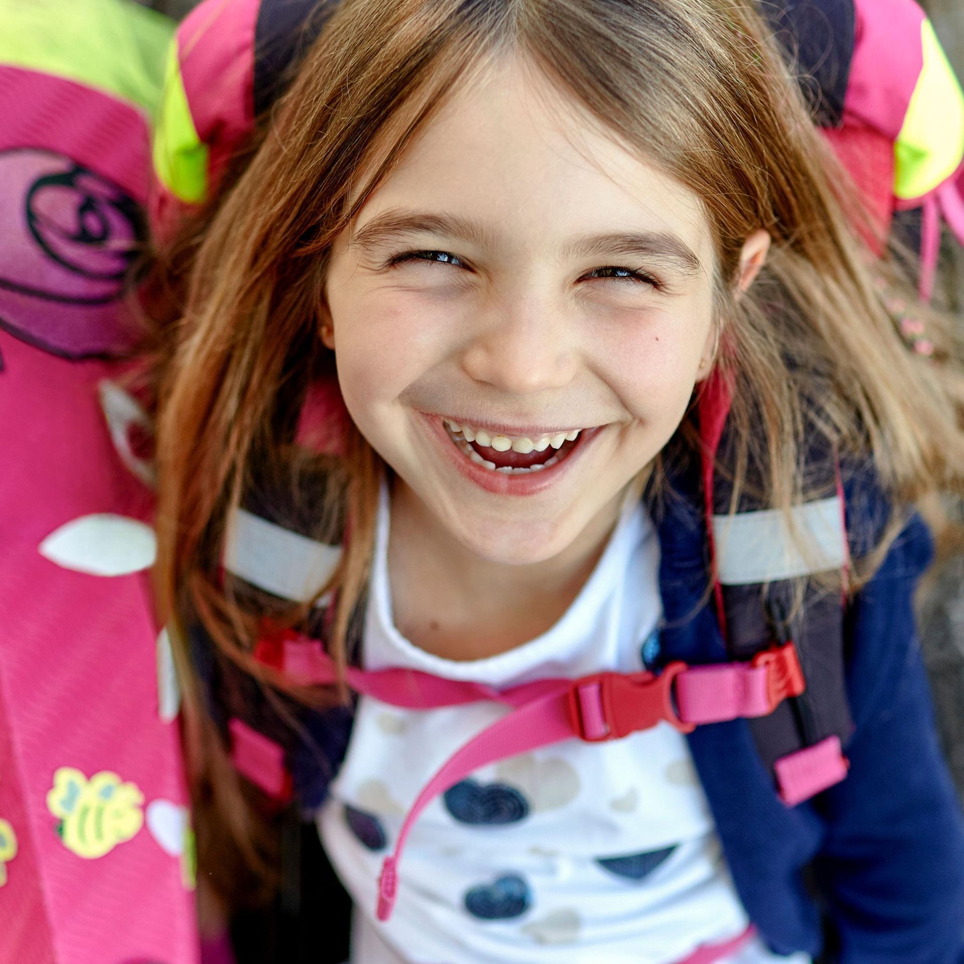 Porträt eines glücklichen Mädchens mit Schultüte und Schulranzen auf Holzplanken