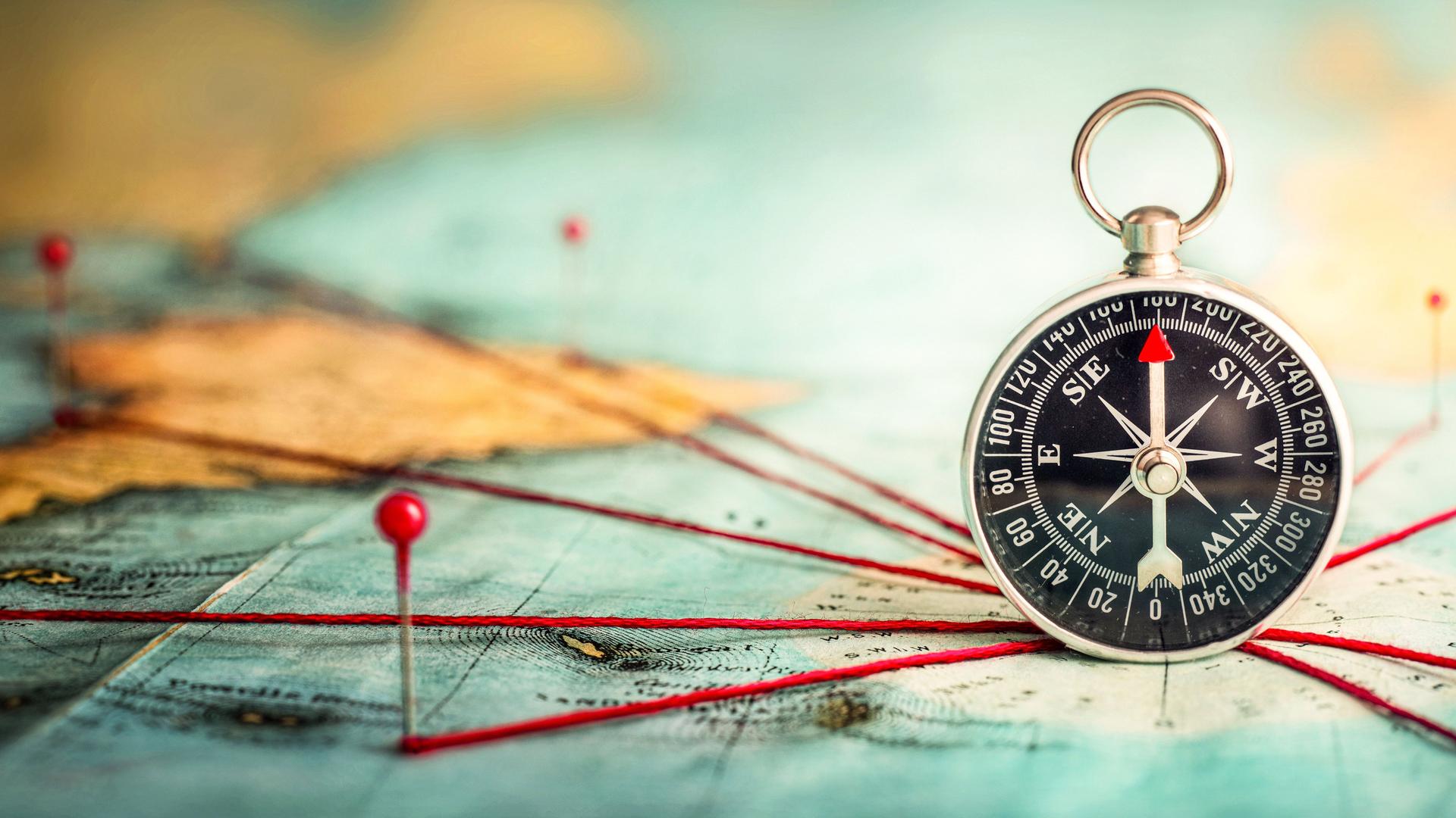 Ein Kompass liegt auf einer Karte. Rote Verbindungsschnüre zeigen in alle Richtungen. 
