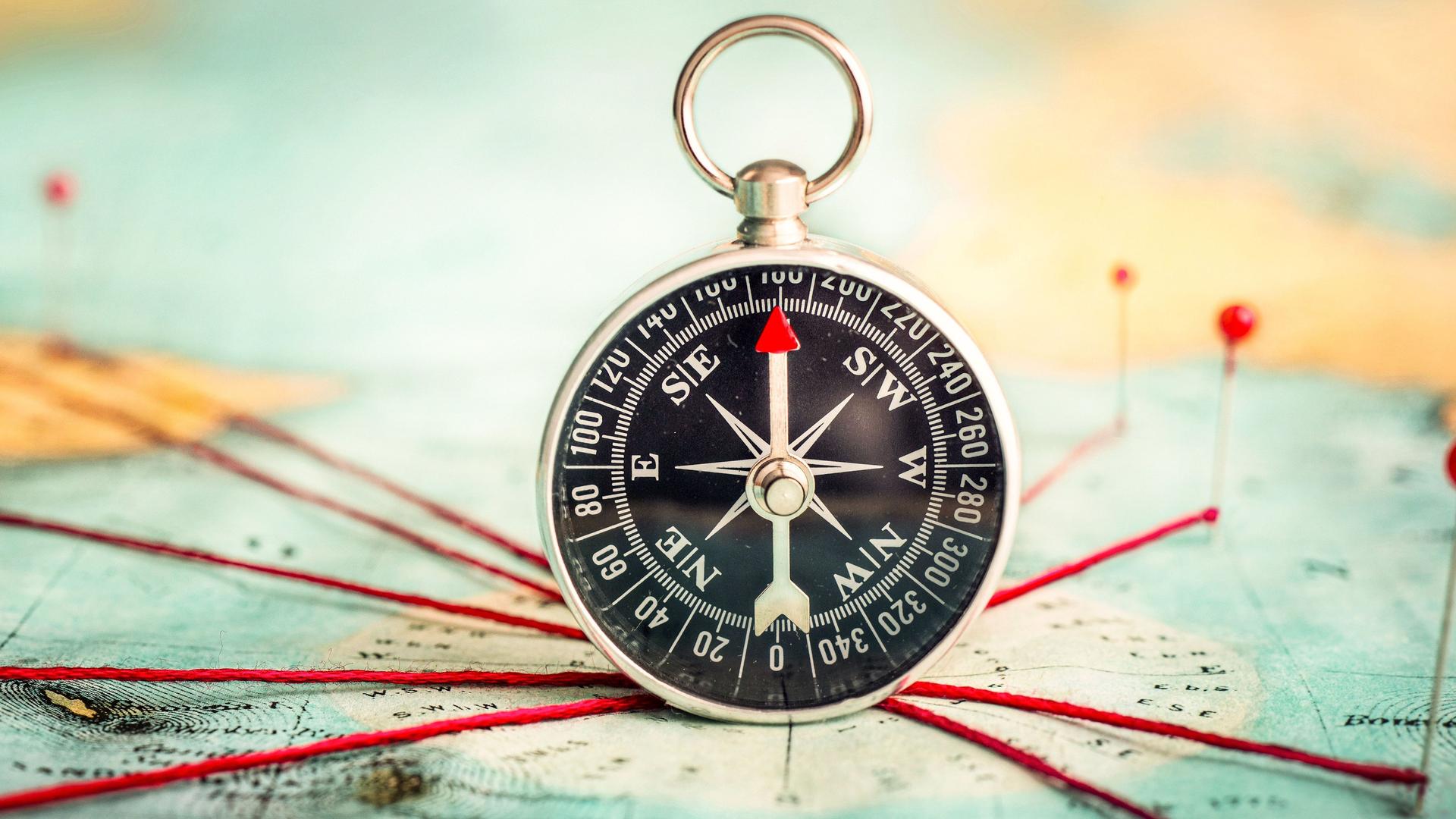 Ein Kompass liegt auf einer Karte. Rote Verbindungsschnüre zeigen in alle Richtungen. 