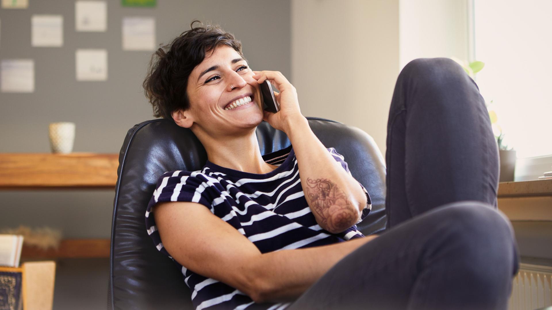 Junge lachende Frau sitzt telefonierend in einem Ledersessel