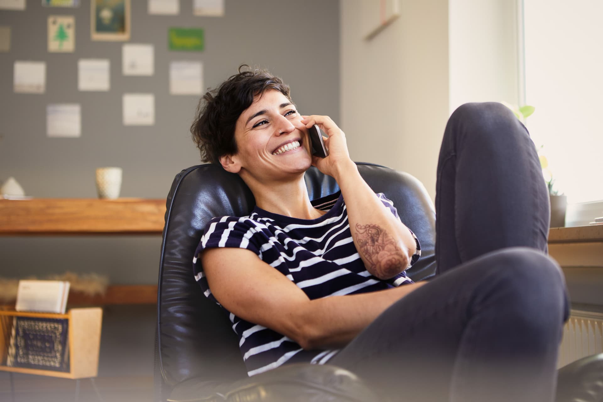 Junge lachende Frau sitzt telefonierend in einem Ledersessel