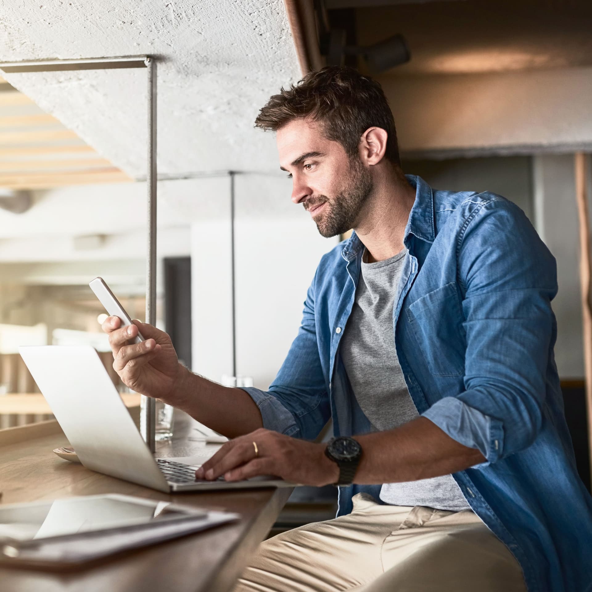 Junger bärtiger Mann arbeitet mit Laptop, Tablet und Handy im Cafe.
