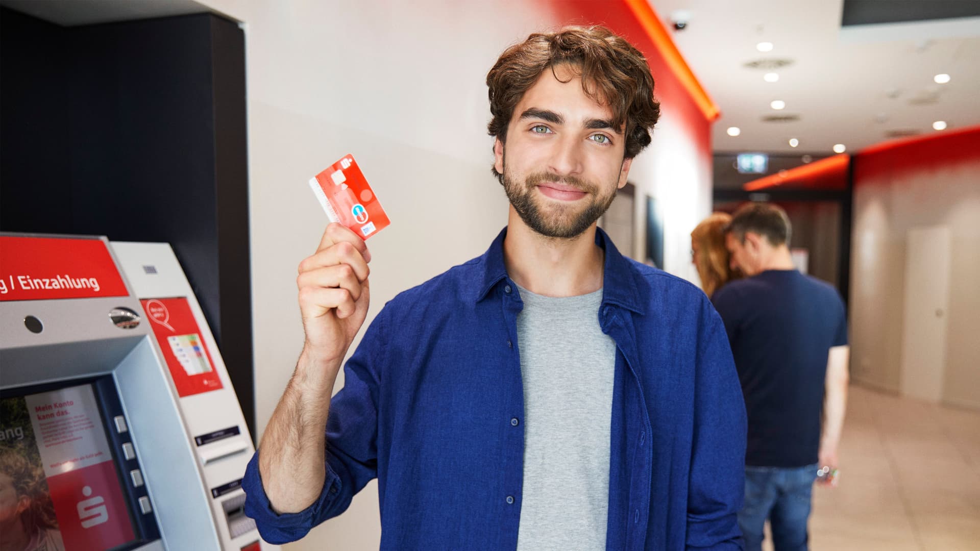 Junger erwachsene zeigt seine Sparkassen EC Kart neben einen Bankautomaten in einer Sparkassen Filiale