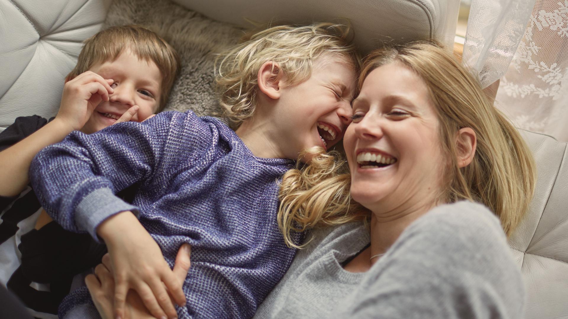 Mutter und zwei Kinder liegen auf ein Sofa und lachen zusammen