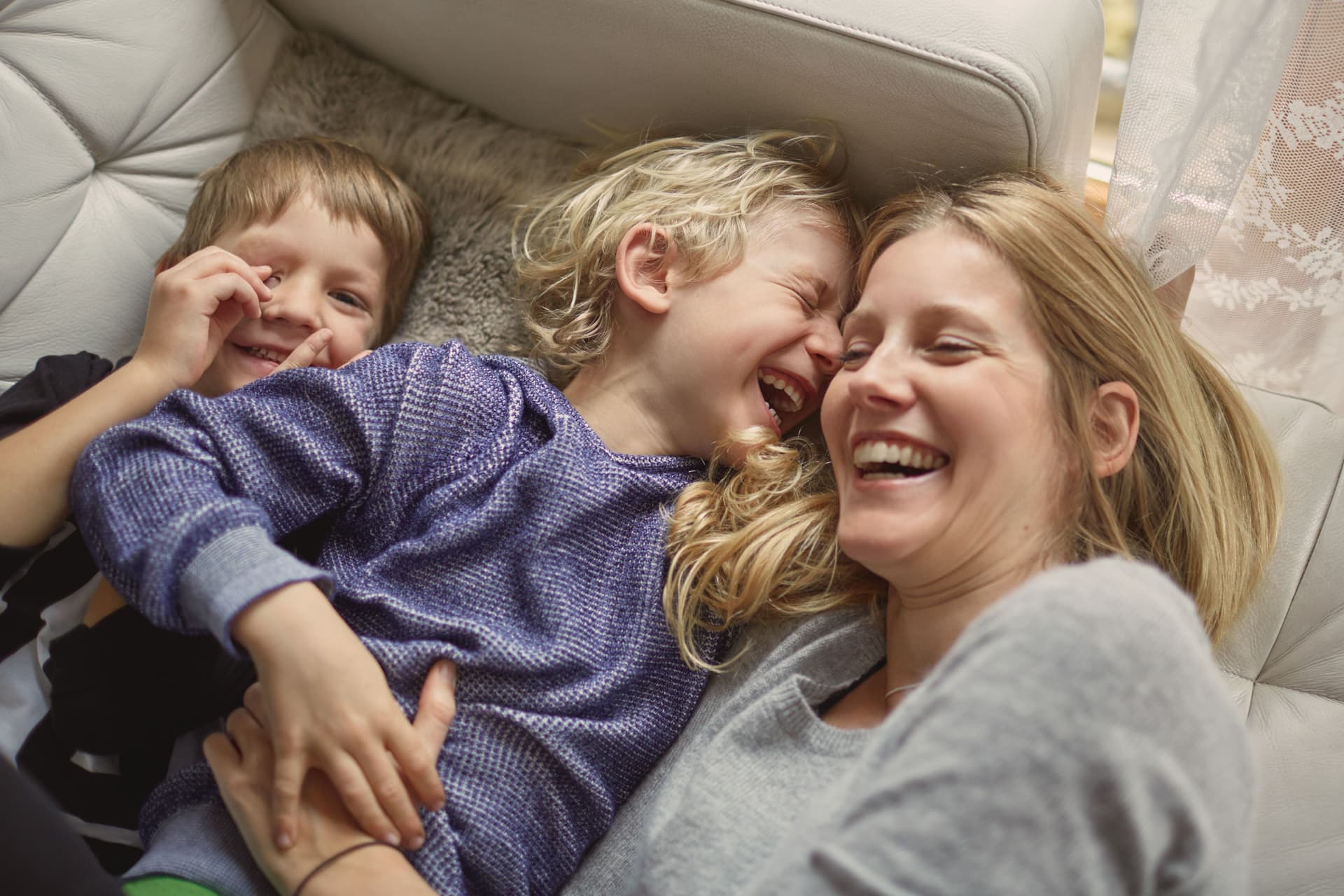 Mutter und zwei Kinder liegen auf ein Sofa und lachen zusammen