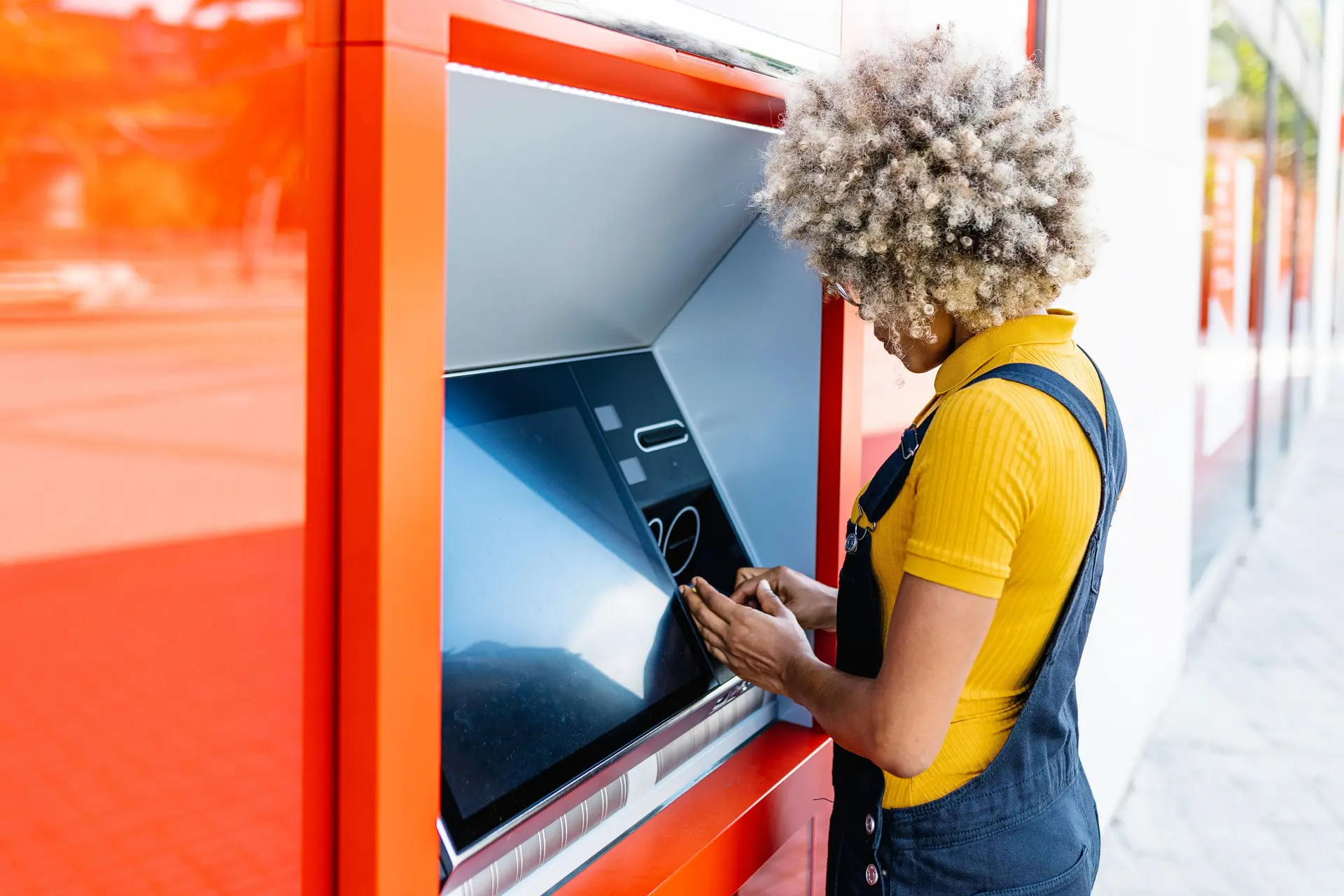 Frau in Latzhose hebt an einem Bankautomat Geld ab