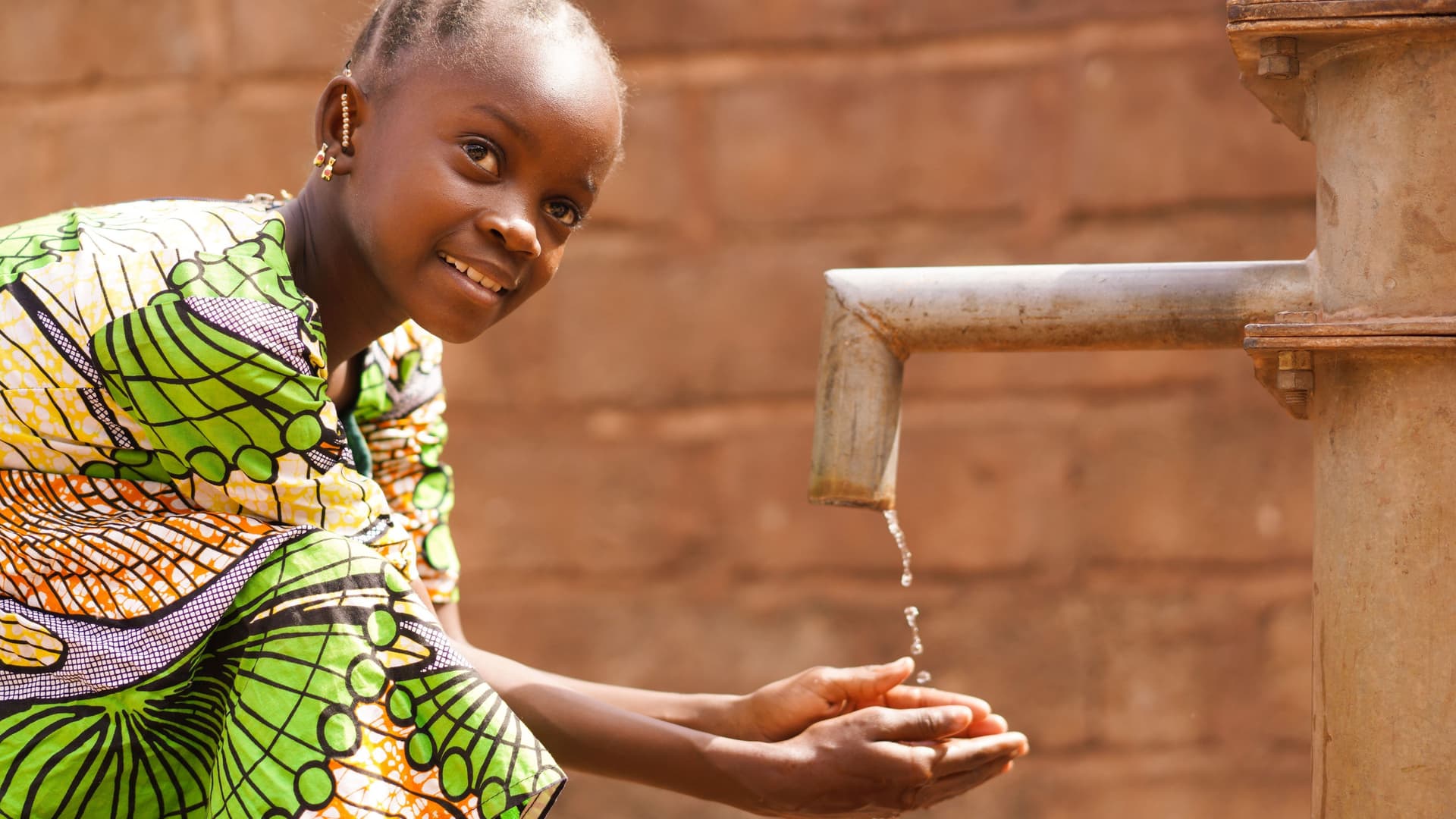 Kind in einem afrikanischen Land wäscht sich an einem Brunnen die Hände und lächelt in die Kamera.