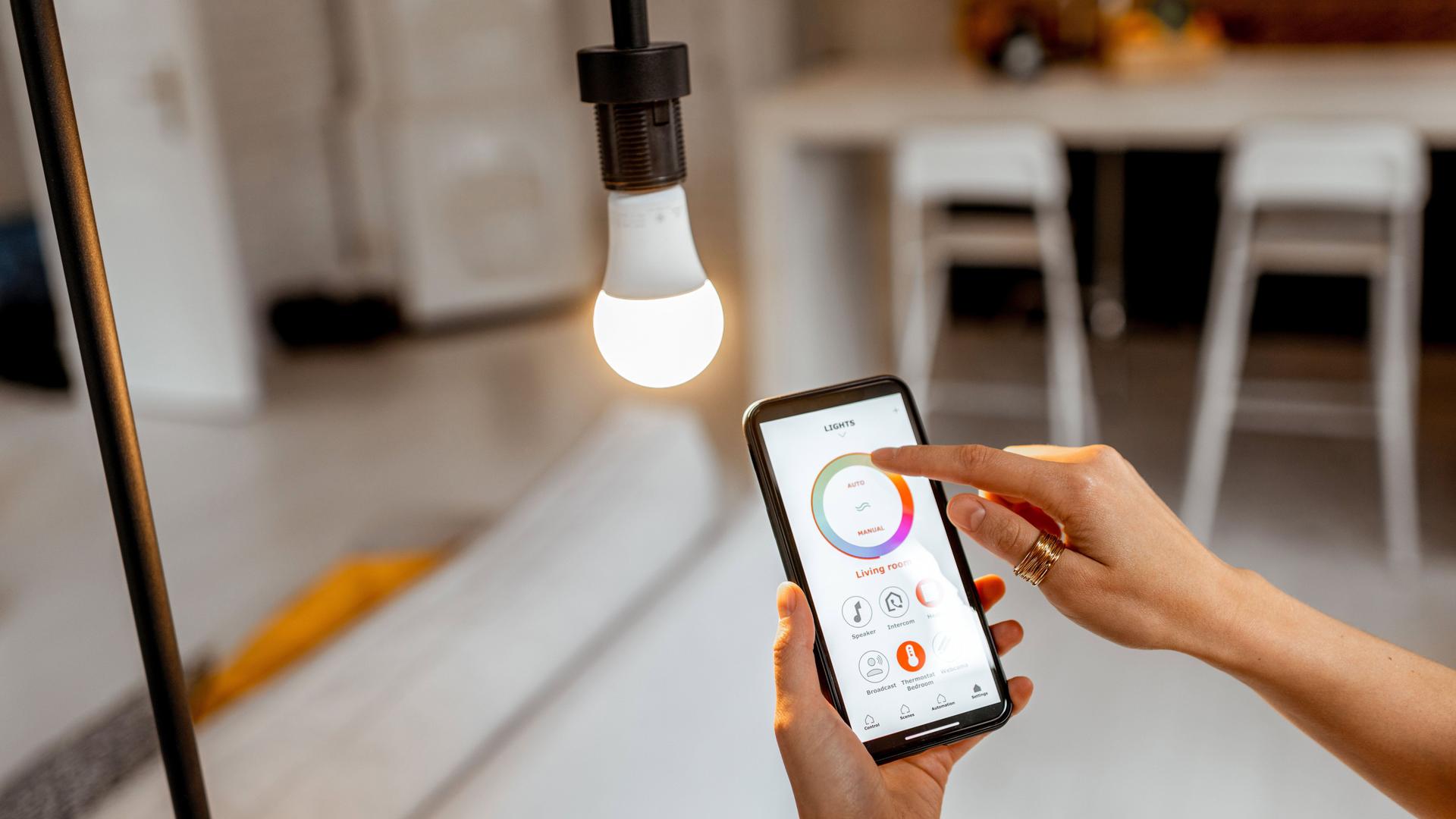 Eine Hand steuert die Temperatur und Intensität einer Glühbirne mit Hilfe einer Smartphone-Anwendung. 