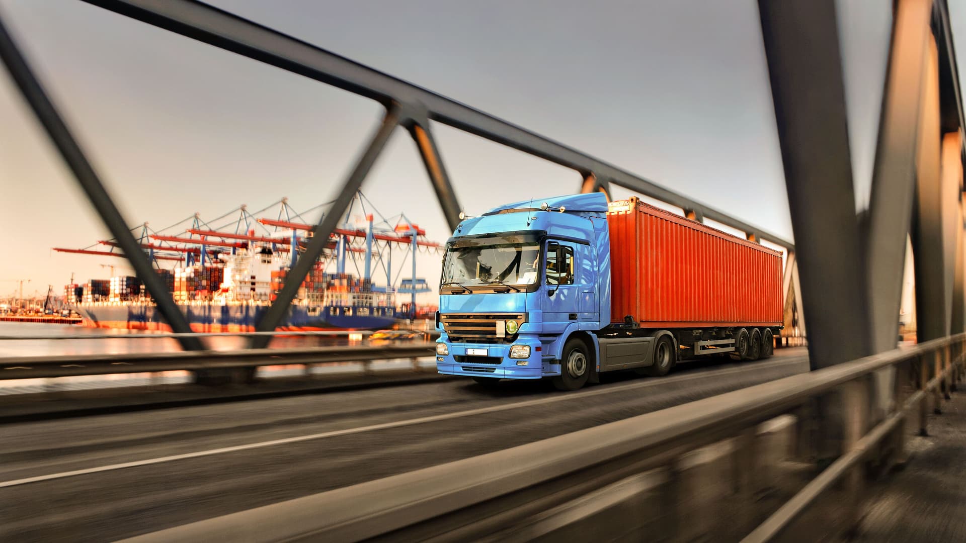 Lastwagen fährt über eine Brücke an einem Containerhafen vorbei.