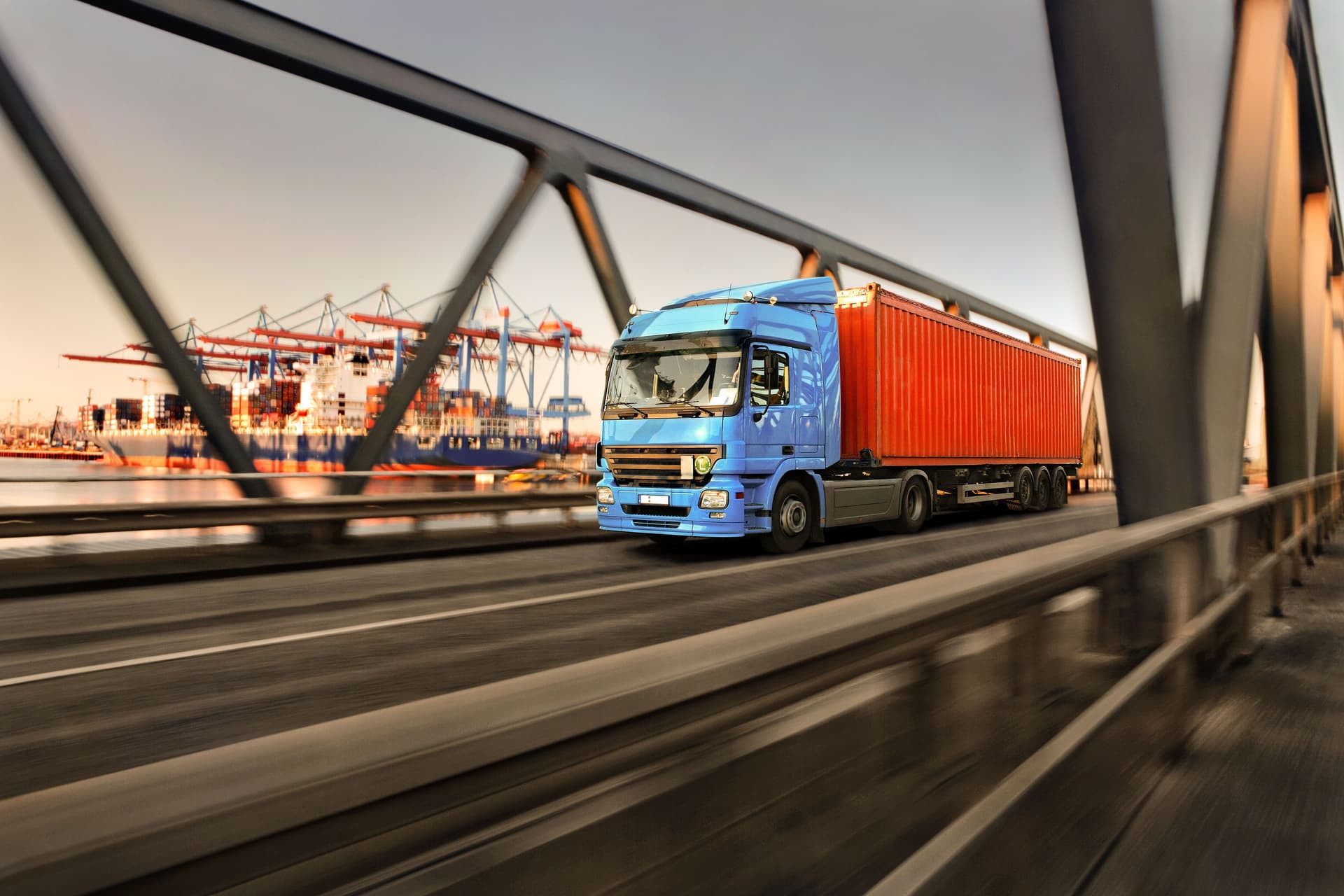 Lastwagen fährt über eine Brücke an einem Containerhafen vorbei.