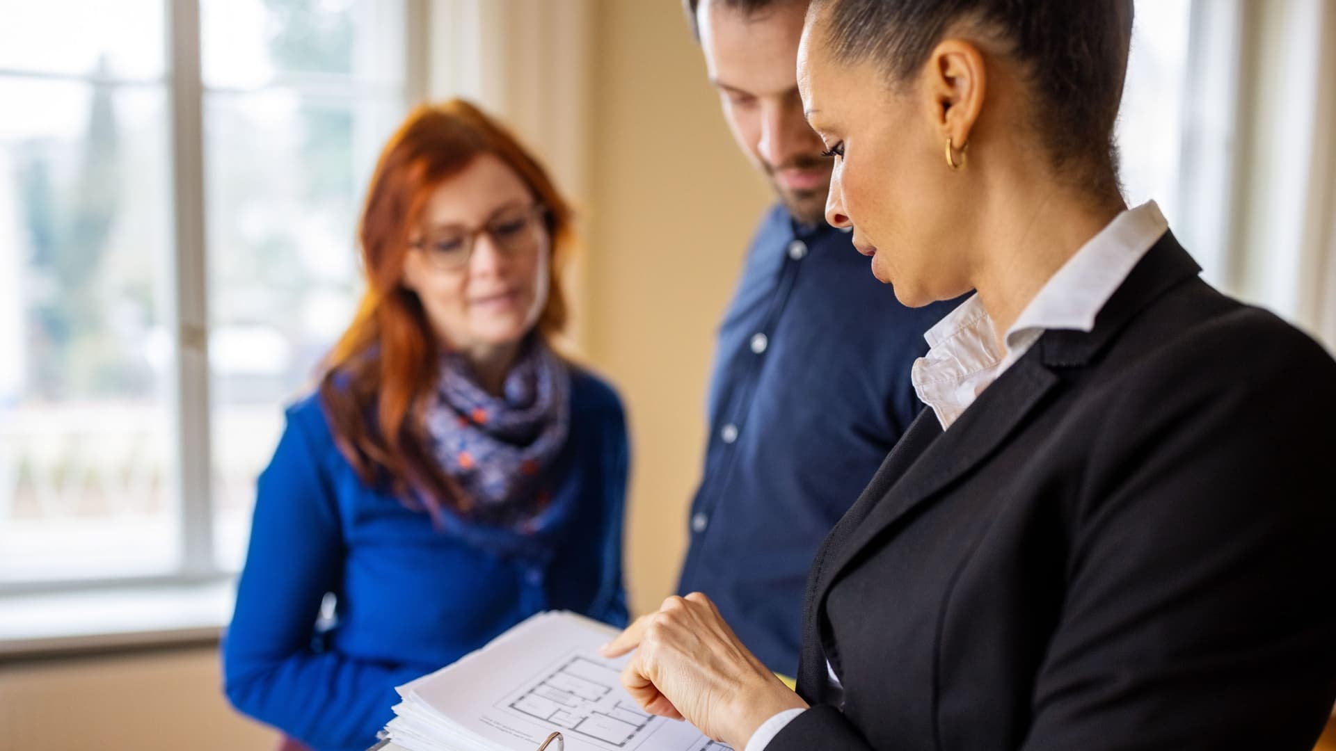 Maklerin bespricht mit einem Paar in einer leeren Wohnung Baupläne.