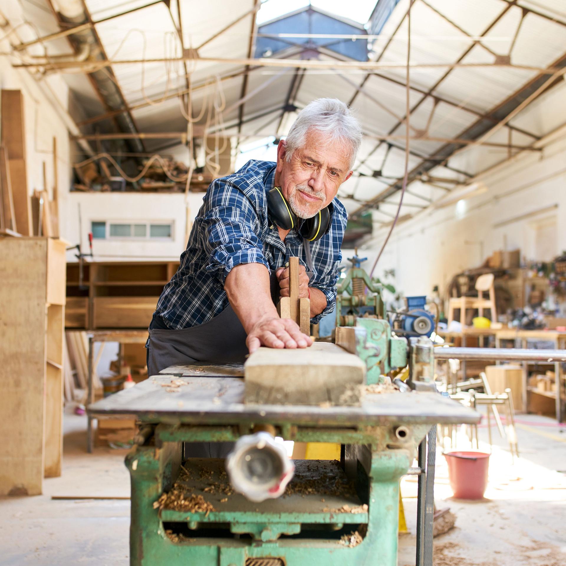 Ein älterer Handwerker arbeitet an der Hobelmaschine in der Werkstatt einer Tischlerei.