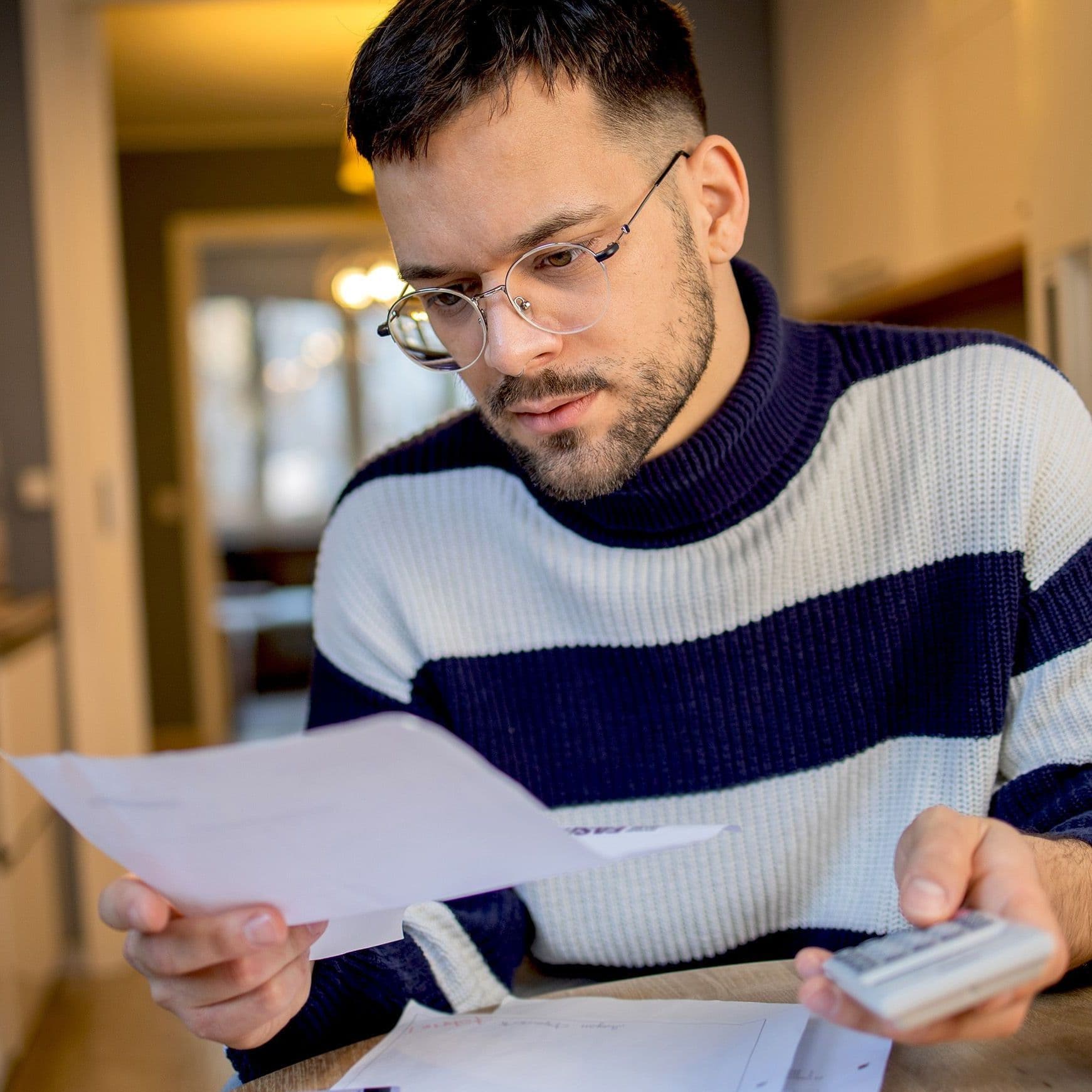Ein Mann begutachtet seine Rechnung. In der anderen Hand hat er einen Taschenrechner.