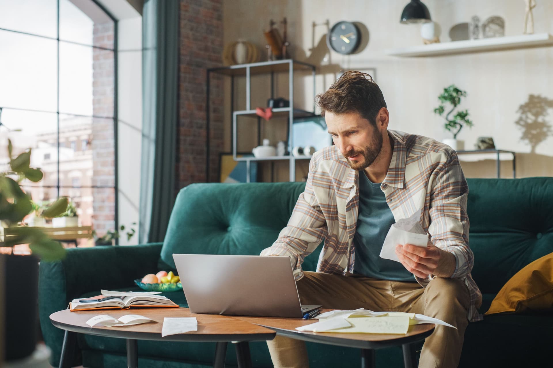 Ein Mann in den dreißigern bezahlt Rechnungen im Online-Banking.Er sitzt auf einer smaragdfarbenen Samt-Couch.