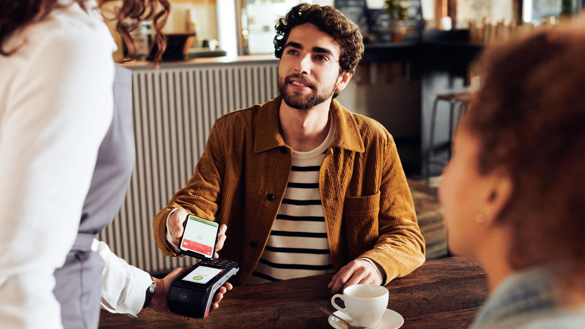 Ein Mann bezahlt mit seinem Smartphone in einem Café.