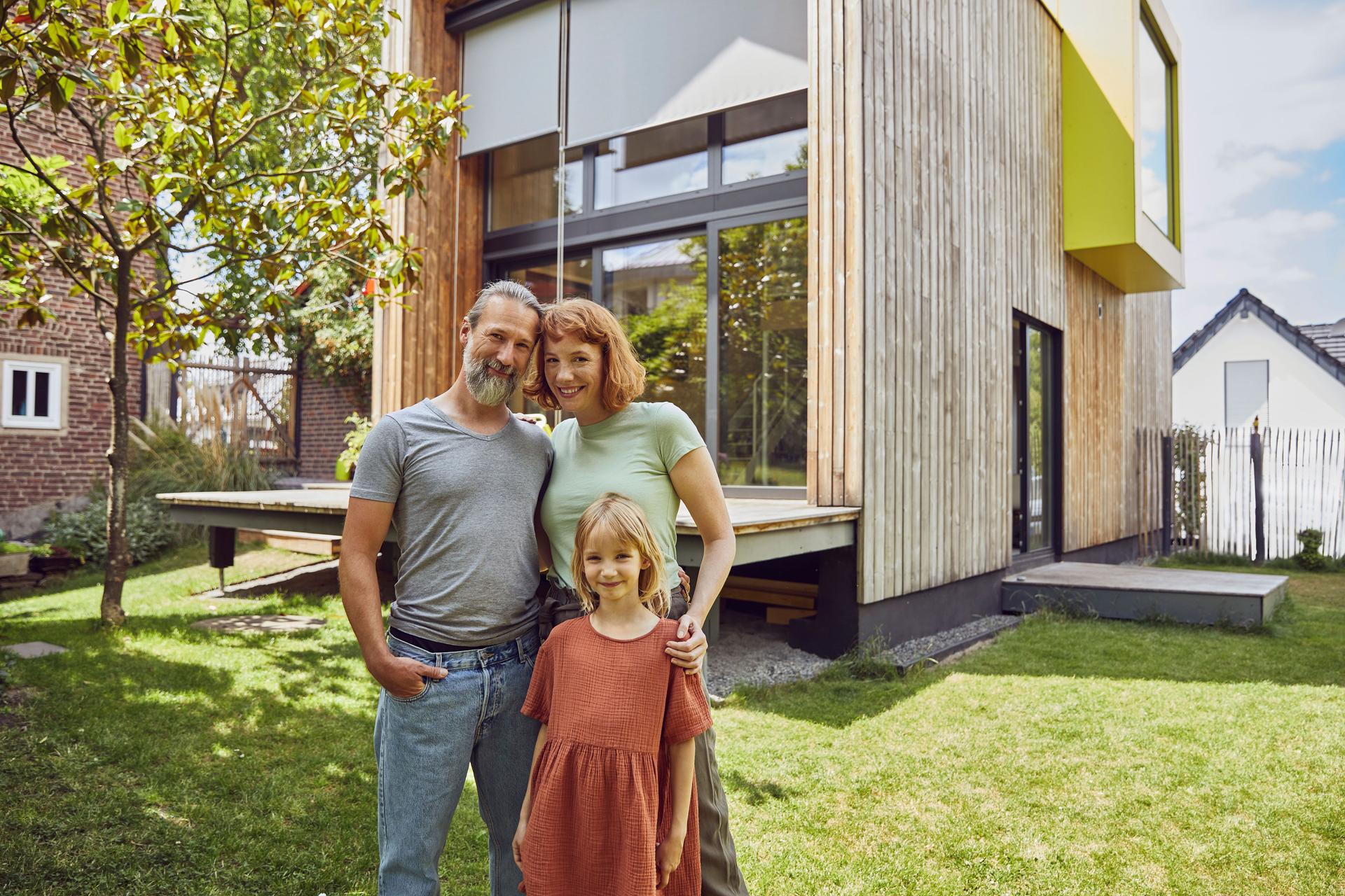 Mann, Frau und Kind stehen in ihrem Garten vor ihrem Holzhaus.