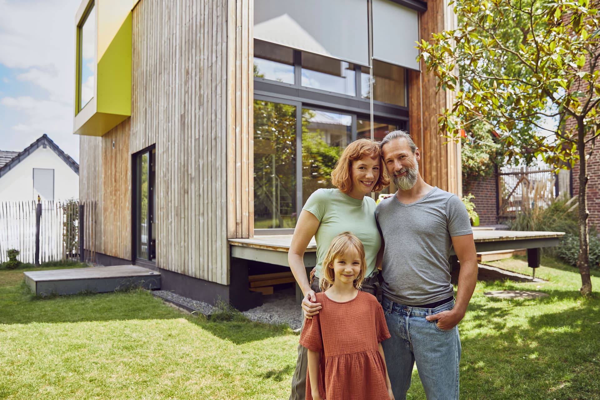 Mann, Frau und Kind stehen in ihrem Garten vor ihrem Holzhaus.