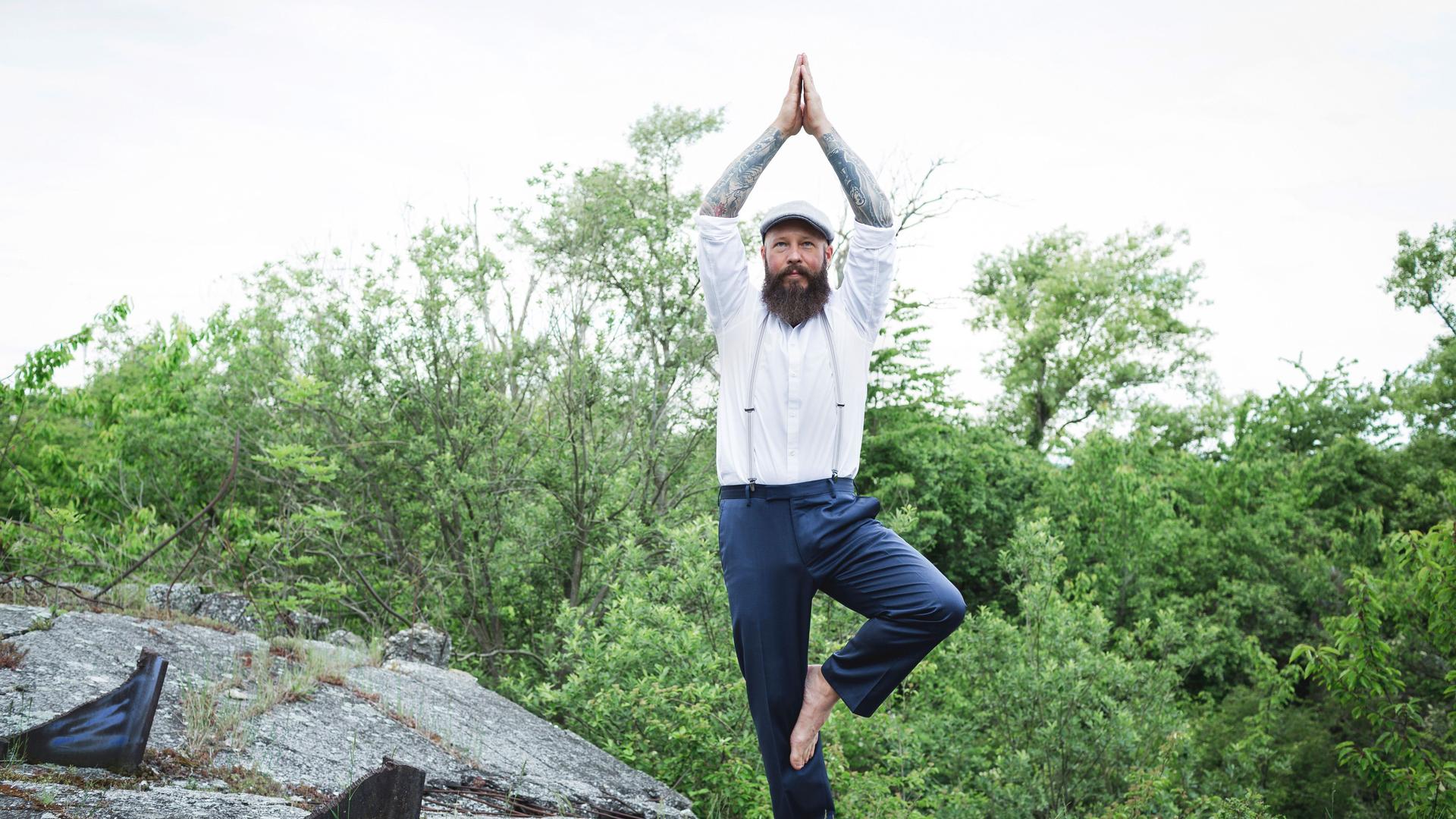 Ein Mann steht auf einem Stein. Er macht Yoga.