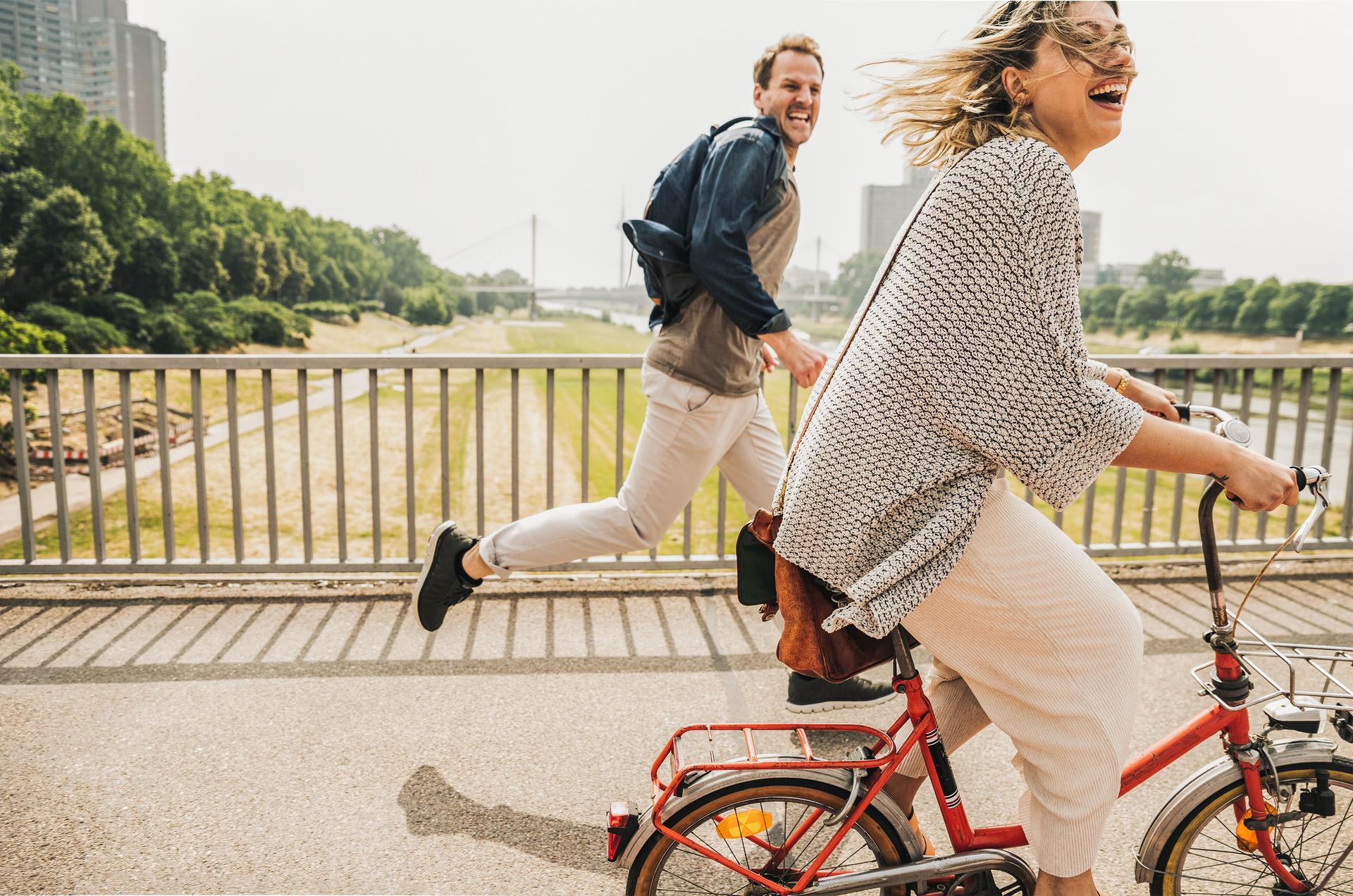 Mann läuft neben einer lachenden Frau, die Fahrrad fährt.