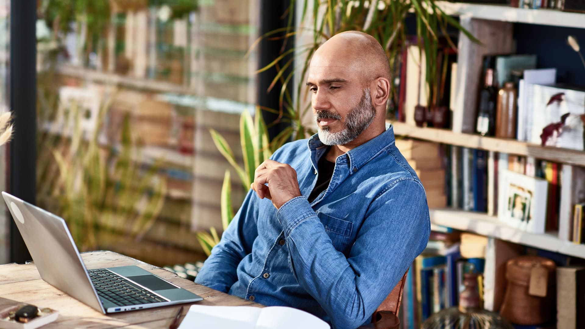 Ein Mann sitzt im Wohnzimmer vor seinem Laptop und blickt nachdenklich auf den Monitor