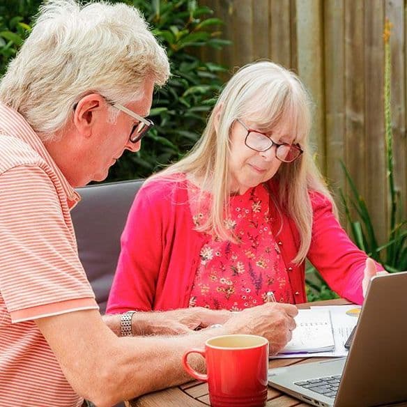 Ein älteres Paar sitzt im Garten und arbeitet gemeinsam an einem Laptop