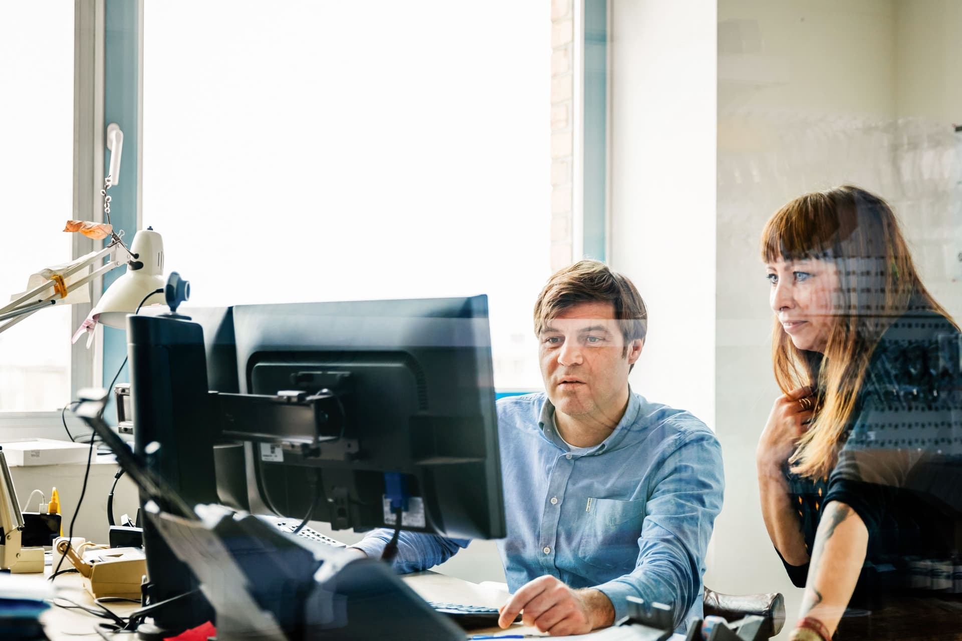Ein Mann und eine Frau blicken im Büro gemeinsam in einen Computermonitor.