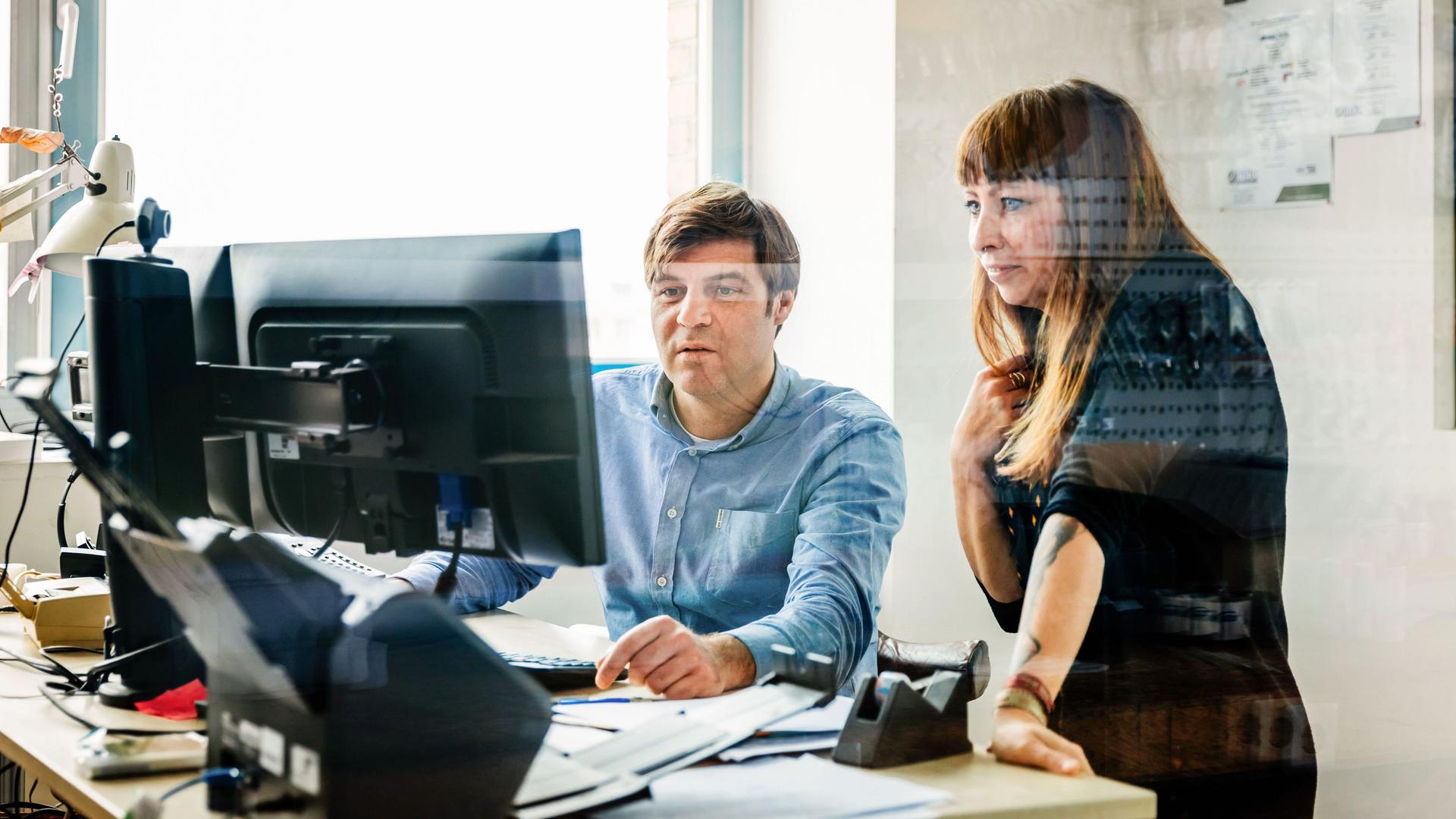 Ein Mann und eine Frau blicken im Büro gemeinsam in einen Computermonitor.