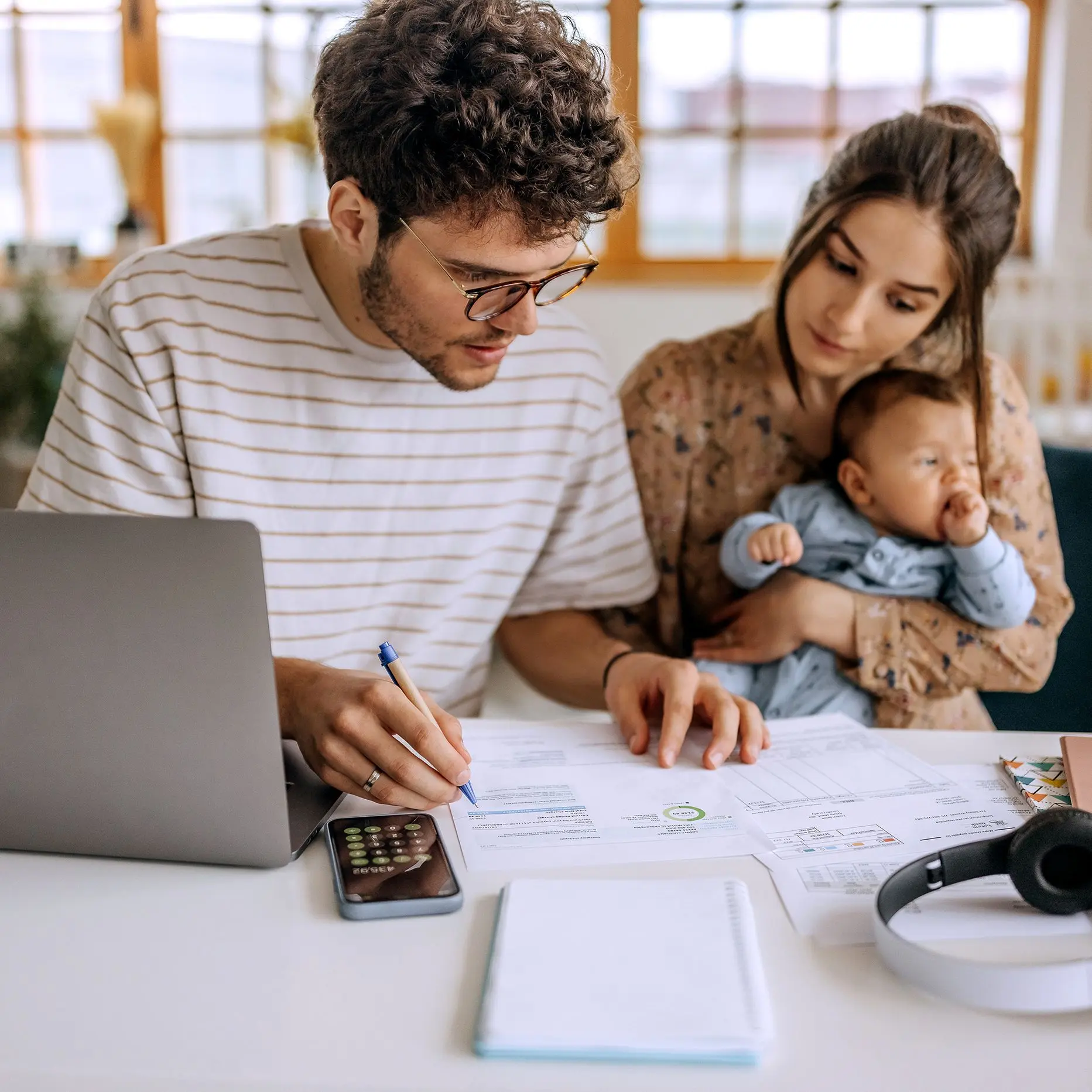 junges Paar mit Baby prüft gemeinsam Unterlagen am Schreibtisch