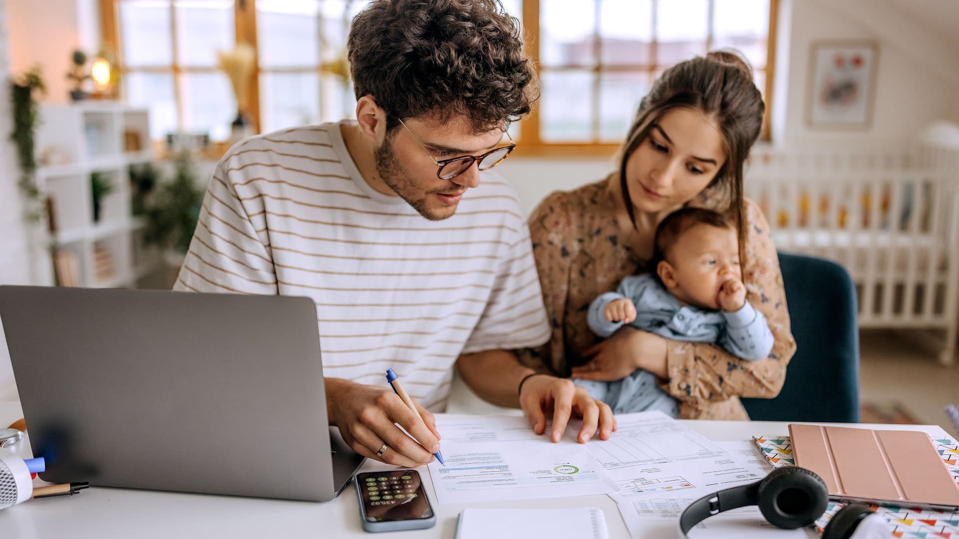 junges Paar mit Baby prüft gemeinsam Unterlagen am Schreibtisch