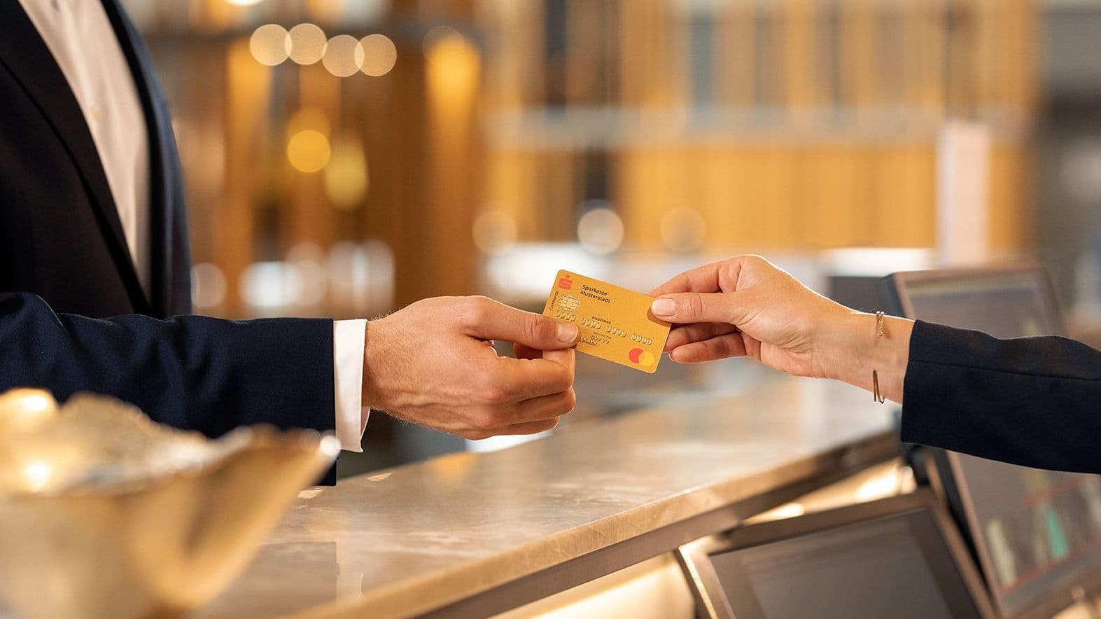 Eine Bankkarte wird von einer männlichen Hand über einen Tresen gereicht und von einer weiblichen Hand gegriffen.