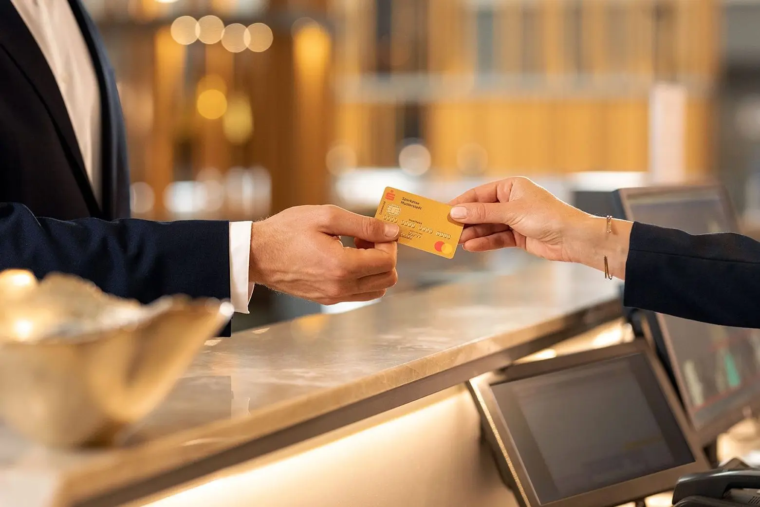 Eine Bankkarte wird von einer männlichen Hand über einen Tresen gereicht und von einer weiblichen Hand gegriffen.