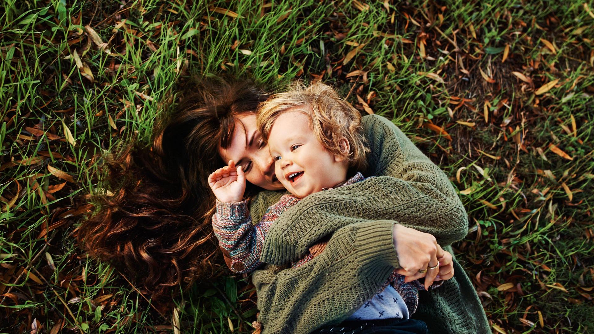 Frau mit lächelnden Kind im Arm, liegend auf einer Wiese.