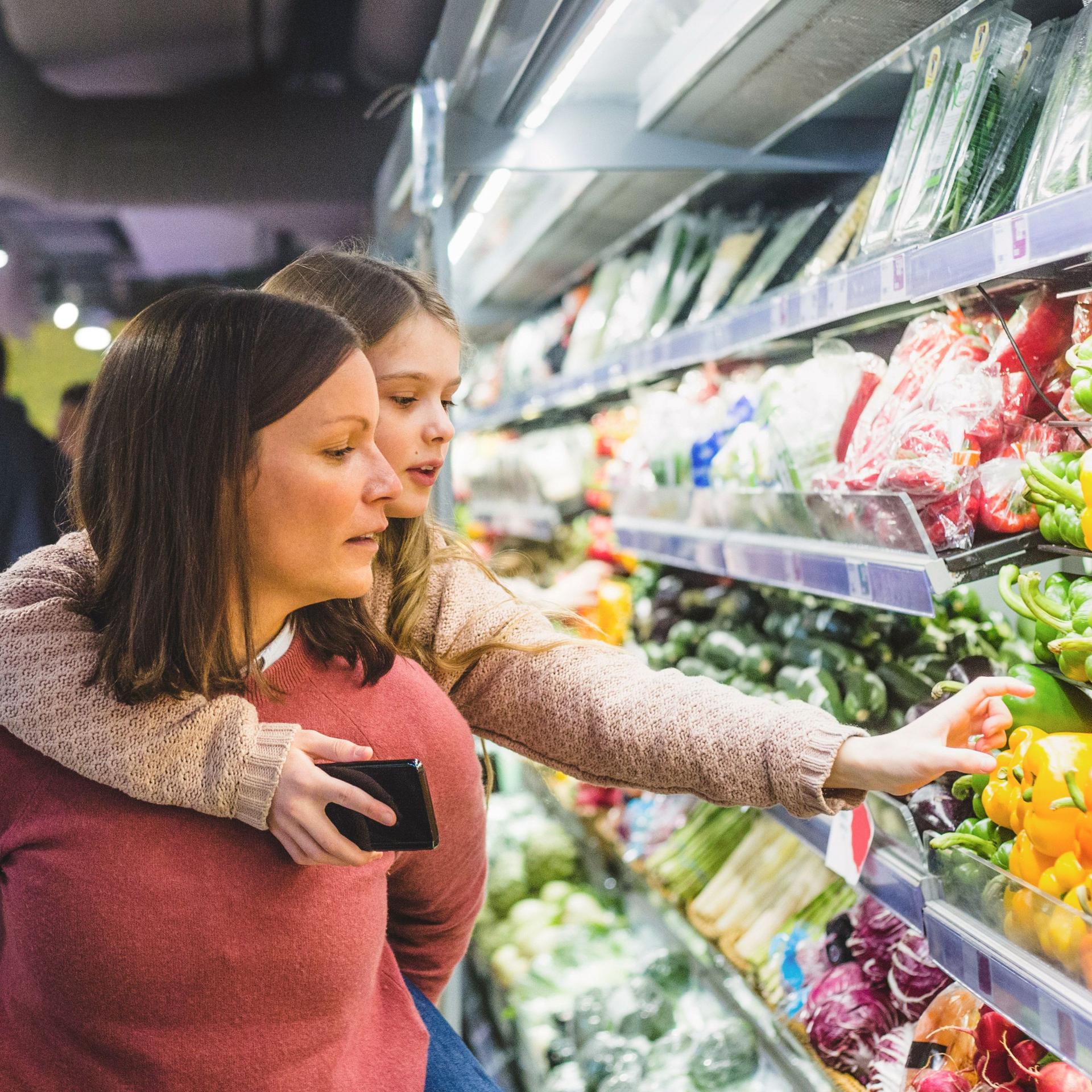Eine Frau trägt ein Mädchen auf dem Rücken in einem Supermarkt in der Gemüseabteilung.