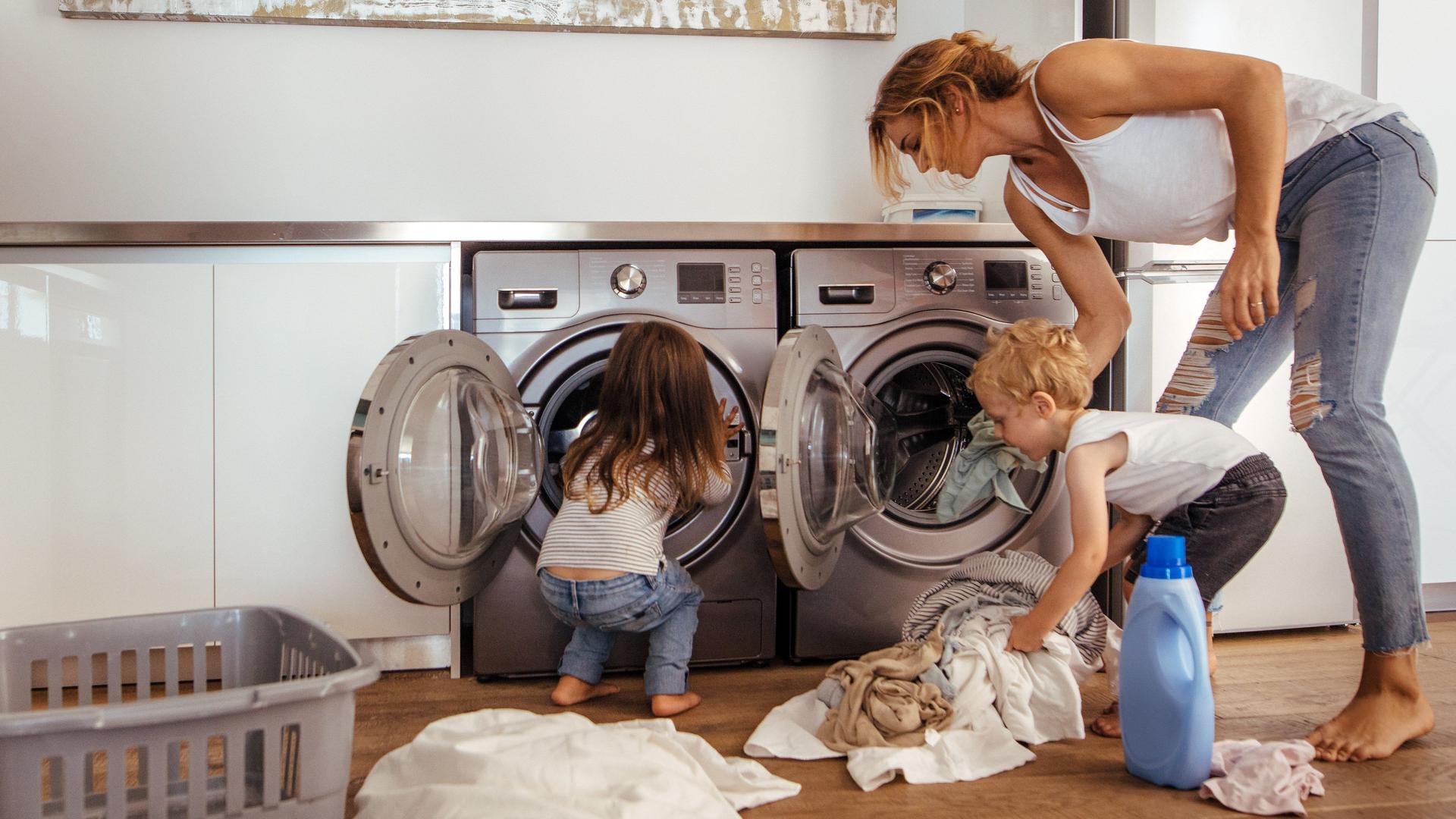 Eine Frau und zwei Kinder befüllen zwei Waschmaschinen in der Wohnküche.